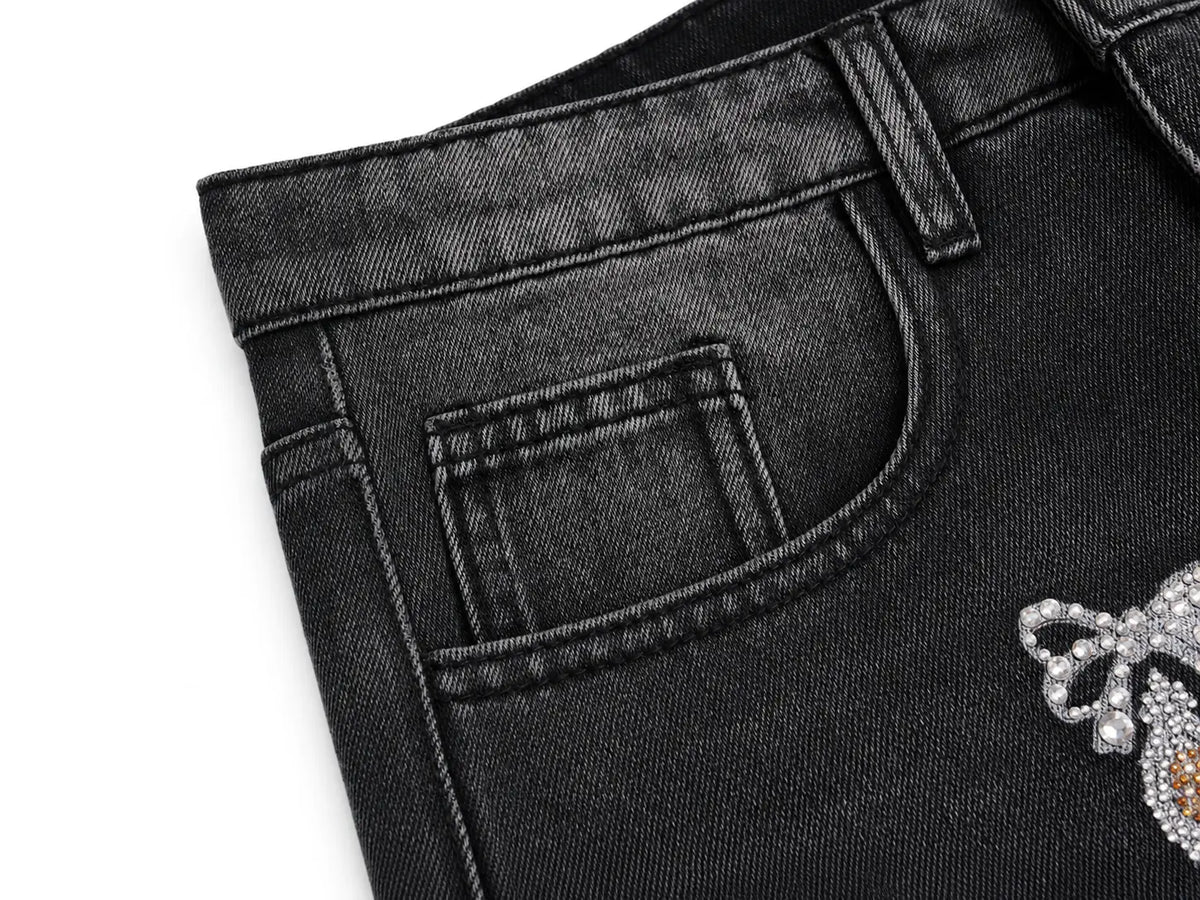 Close-up of a pair of black denim jeans showing the back pocket, belt loop, and a rhinestone-embellished bow detail on the right leg, set against a plain white background. TCH Rhinestone Bow & Butterfly Flare Jeans