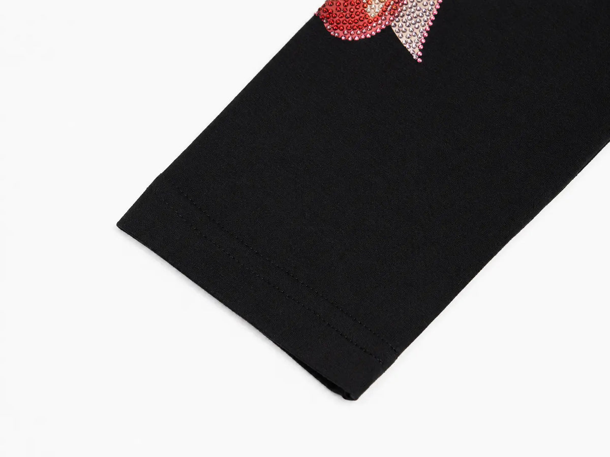 Close-up of a black sleeve featuring a decorative red and silver rhinestone bow design near the cuff, set against a plain white background. TCH Rhinestone Bow Cherry Drawstring Long Sleeve Top