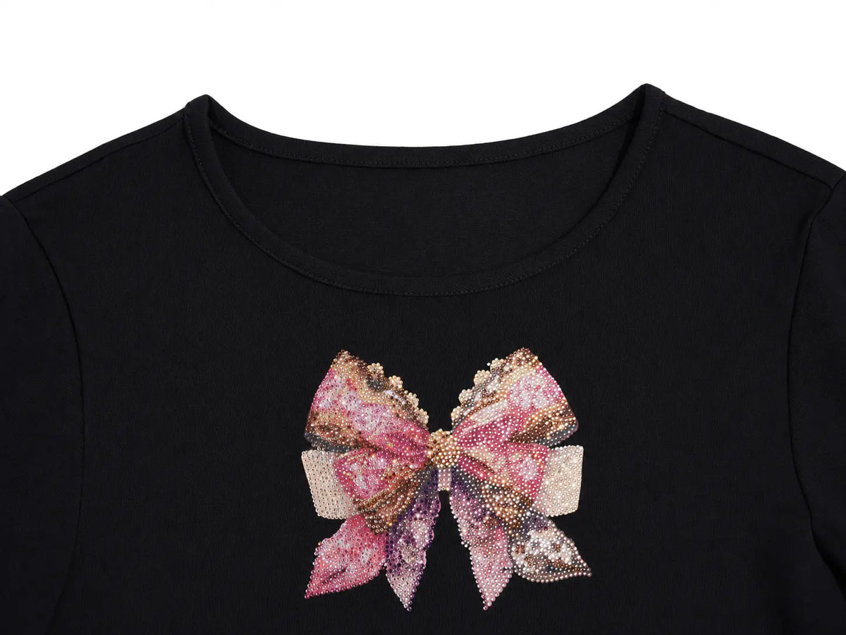 Close-up of a black crewneck top featuring a large, decorative sequined bow graphic on the chest in shades of pink, gold, and silver. TCH Rhinestone Bow Cherry Drawstring Long Sleeve Top