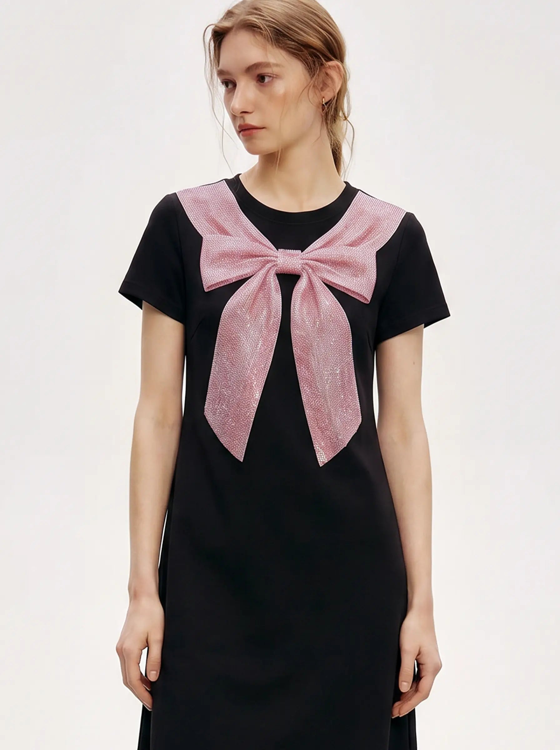 A model wearing a black short-sleeve dress with a large pink bow detail on the chest, set against a plain light gray studio background. TCH Rhinestone Bow Collar Black Mini Dress