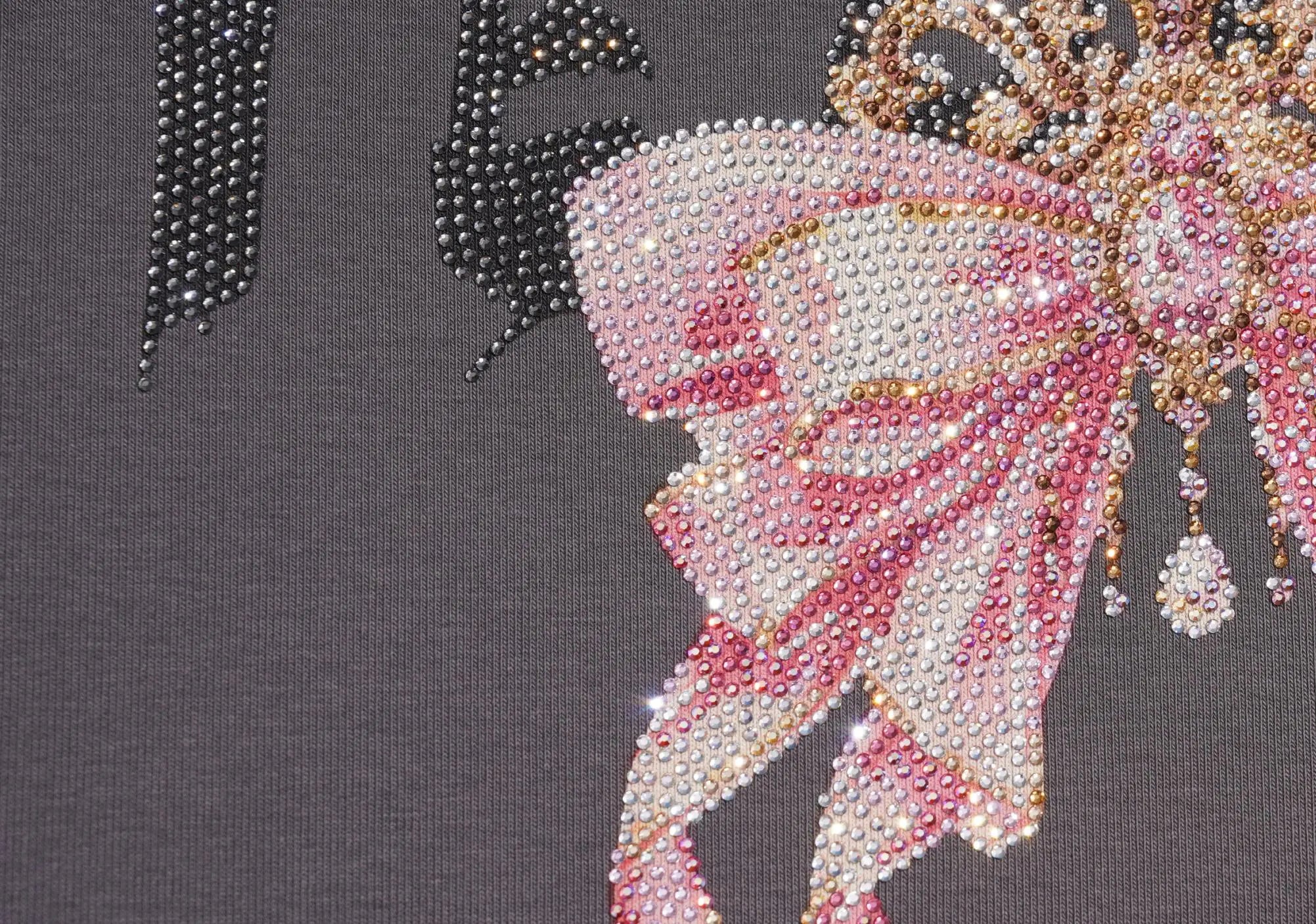 Close-up of a dark gray fabric featuring a large pink and white rhinestone bow design with gold-toned embellishments and partial black lettering. TCH Rhinestone Bow Crown Graphic Mini Dress
