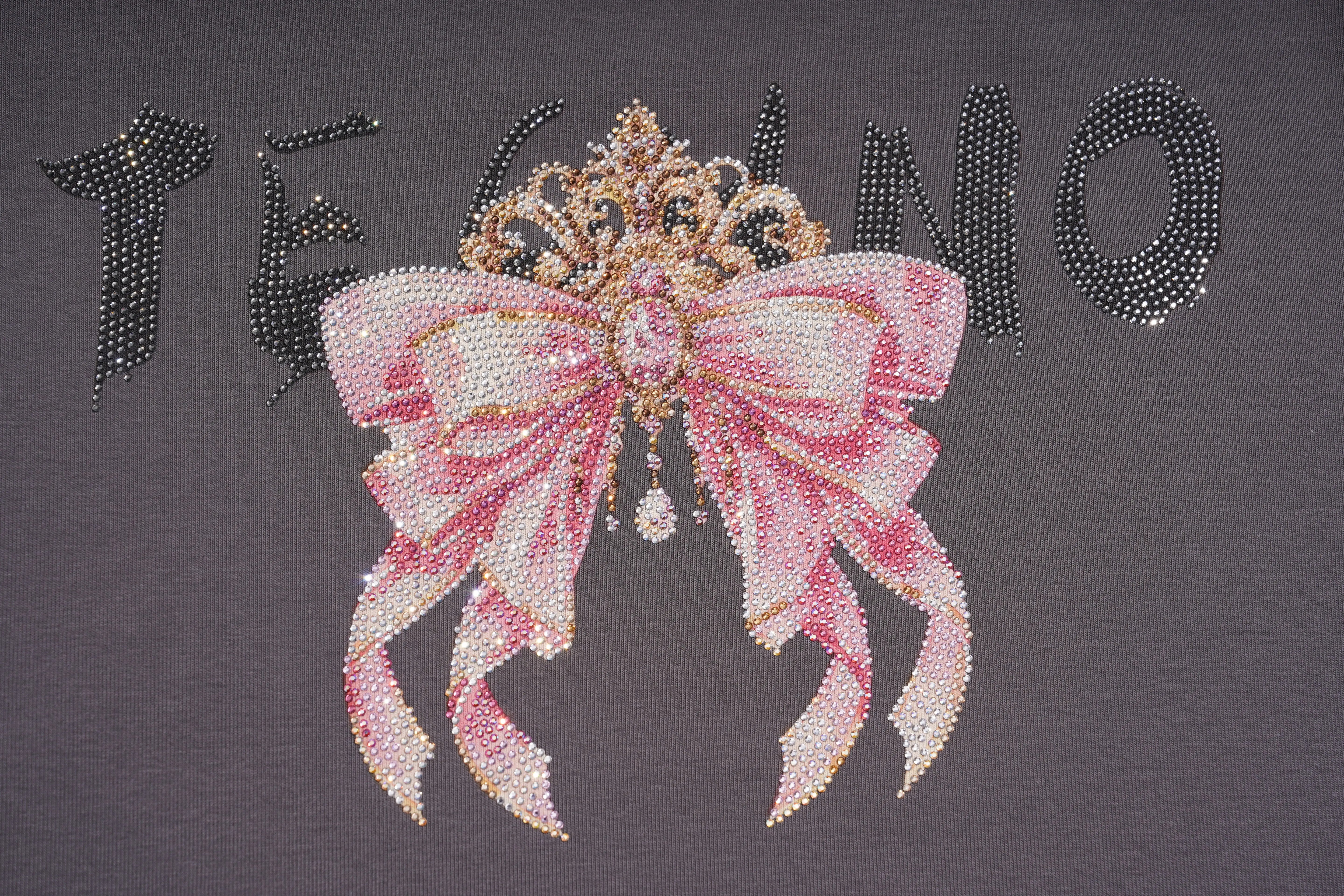 A close-up of a dark gray garment featuring a large pink rhinestone bow graphic with a jeweled tiara and black rhinestone lettering behind it. TCH Rhinestone Bow Crown Graphic Mini Dress