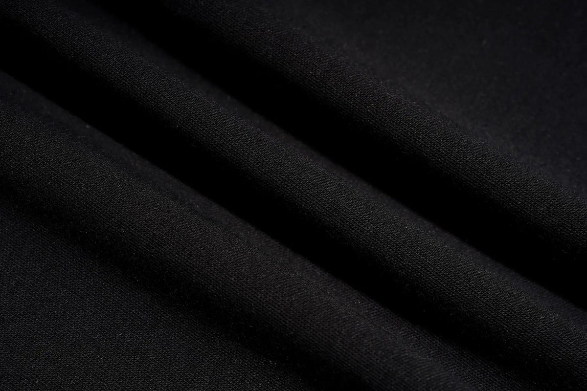 A close-up of draped black fabric with soft folds showing a fine woven texture. TCH Rhinestone Bow Graphic Fitted Long Sleeve Top