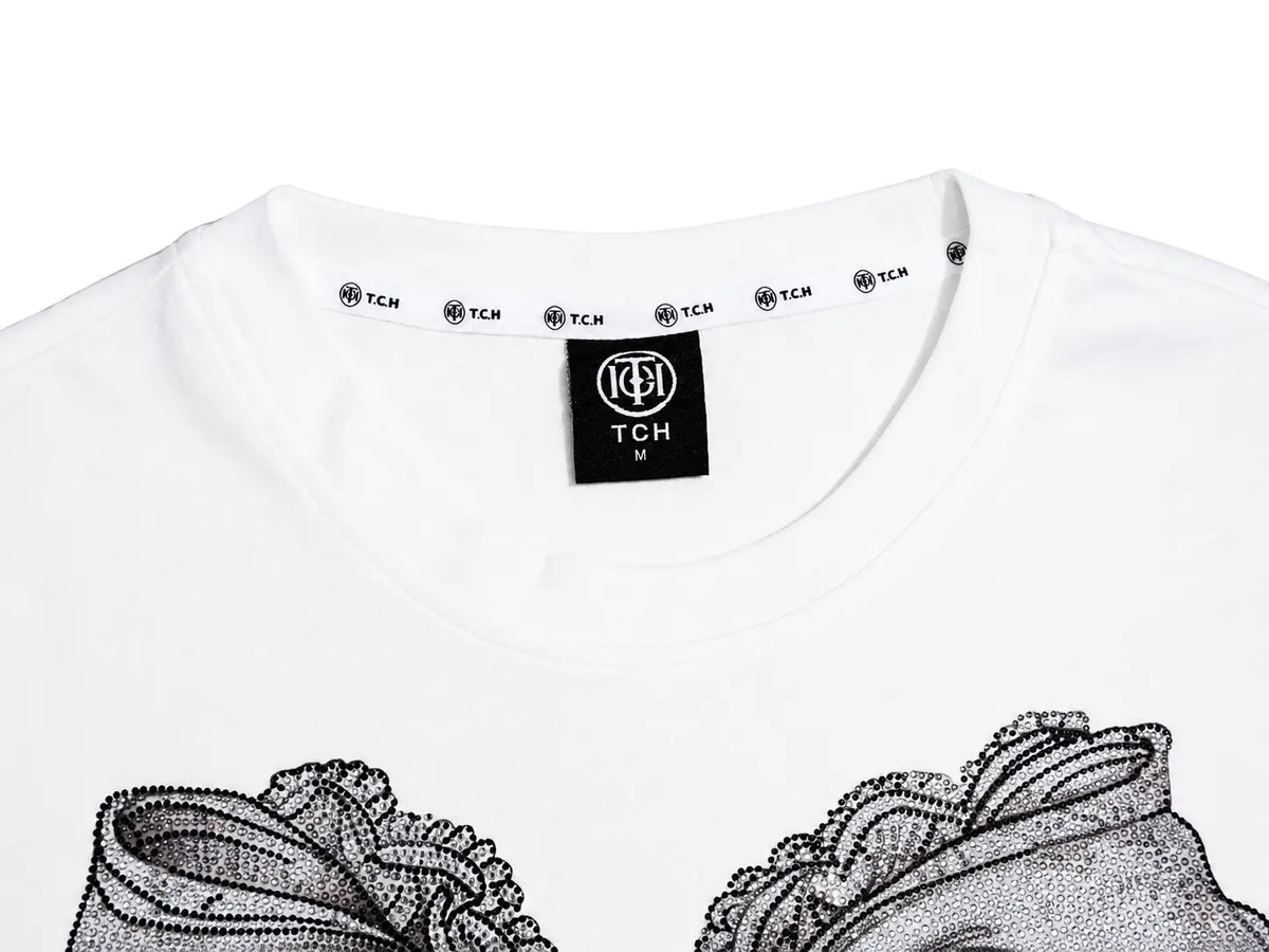 Close-up of a white T-shirt neck area showing a black TCH brand label inside the collar and part of a black graphic print at the bottom. TCH Rhinestone Bow Graphic Fitted Long Sleeve Top