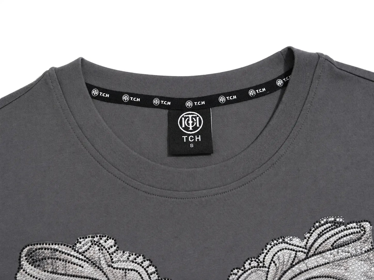 Close-up of a dark gray crewneck t-shirt featuring a black neck label with the TCH logo and white sequined floral patterns on the front. TCH Rhinestone Bow Graphic Fitted Long Sleeve Top