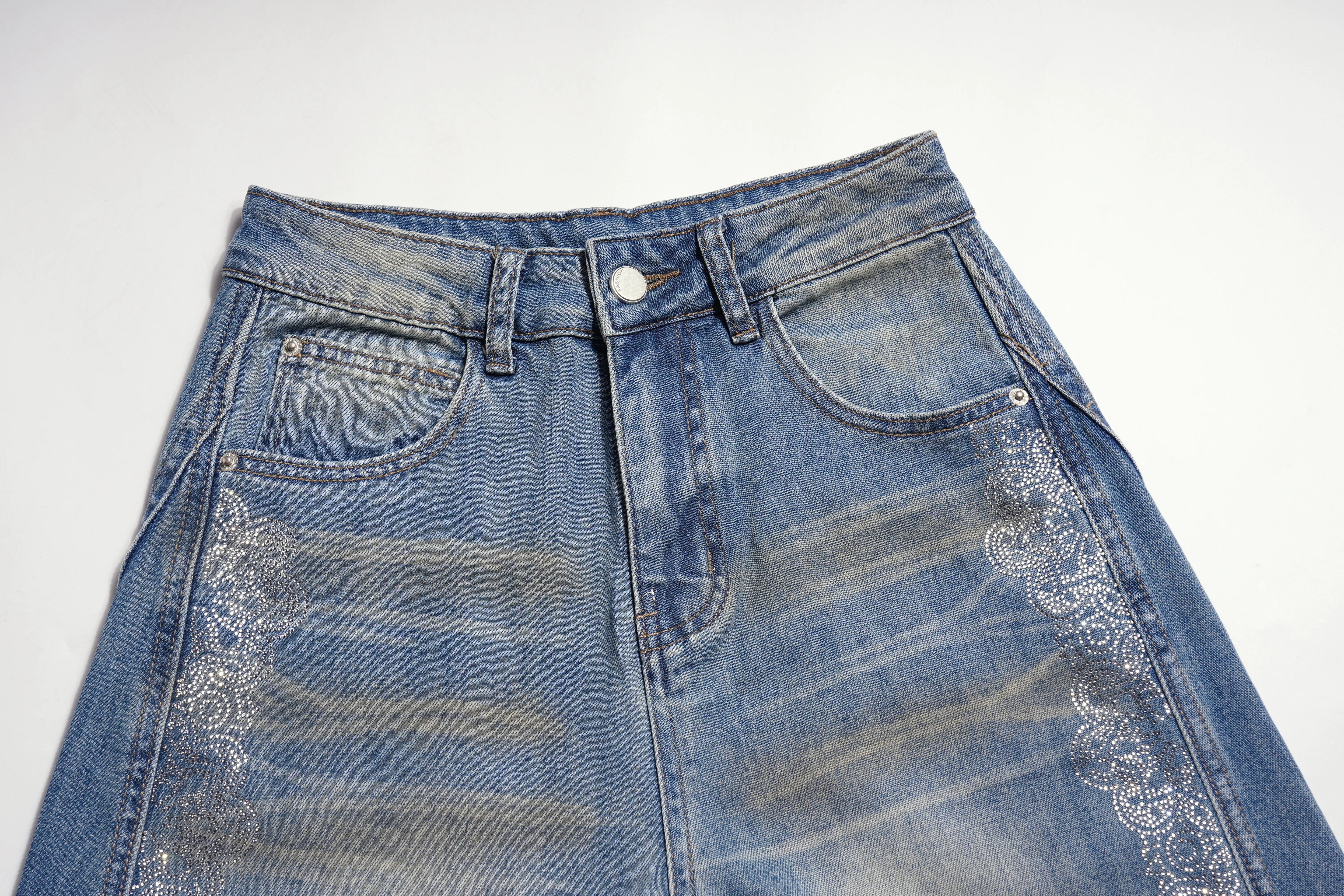 A close-up of a blue denim skirt with decorative white embroidered lace-like patterns on the sides, shown against a plain white background. TCH Rhinestone Bow Lace Side Panel Wide Leg Jeans
