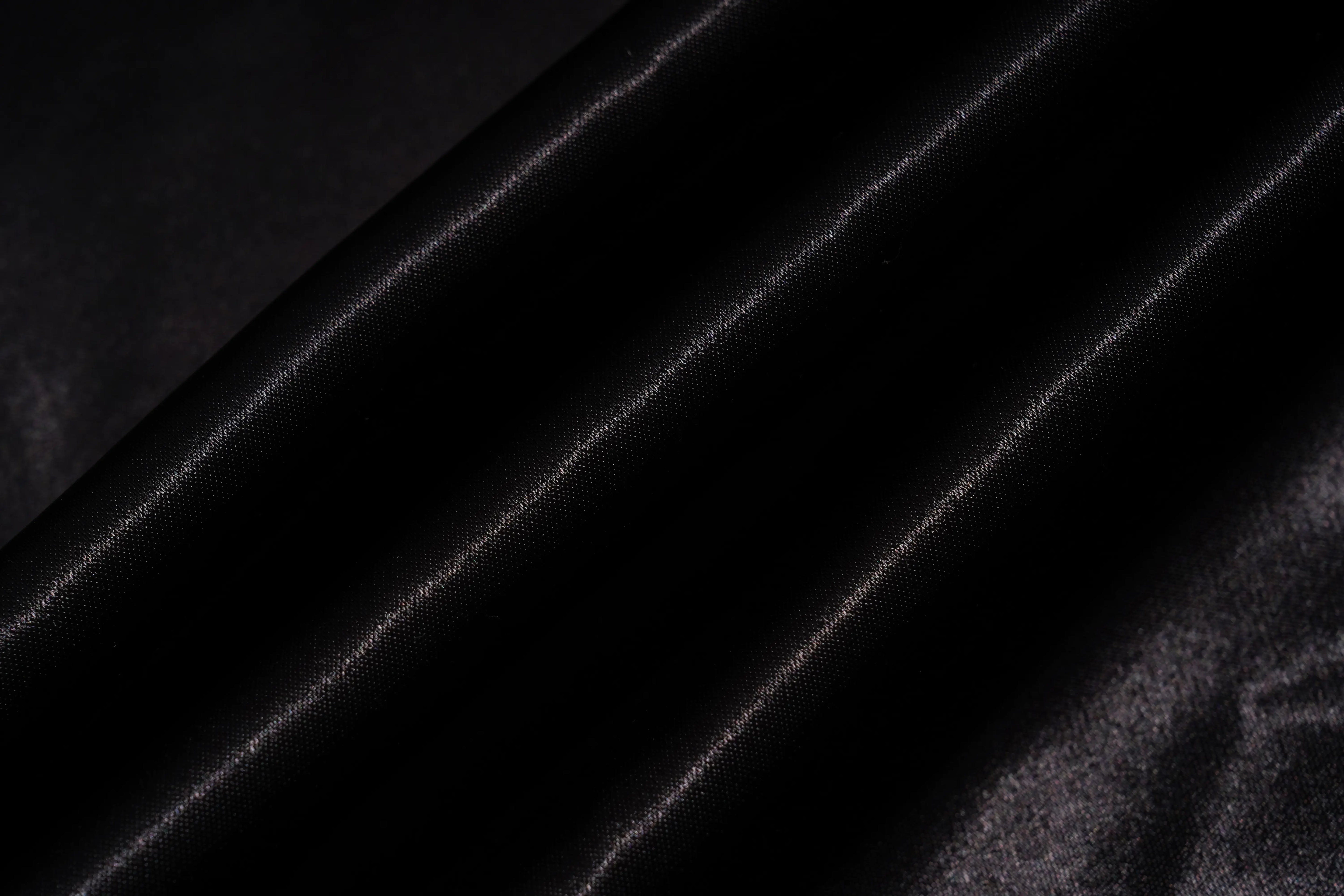 A close-up of draped black fabric with a subtle sheen, showing diagonal folds and a smooth texture. TCH Rhinestone Bow Satin Blazer
