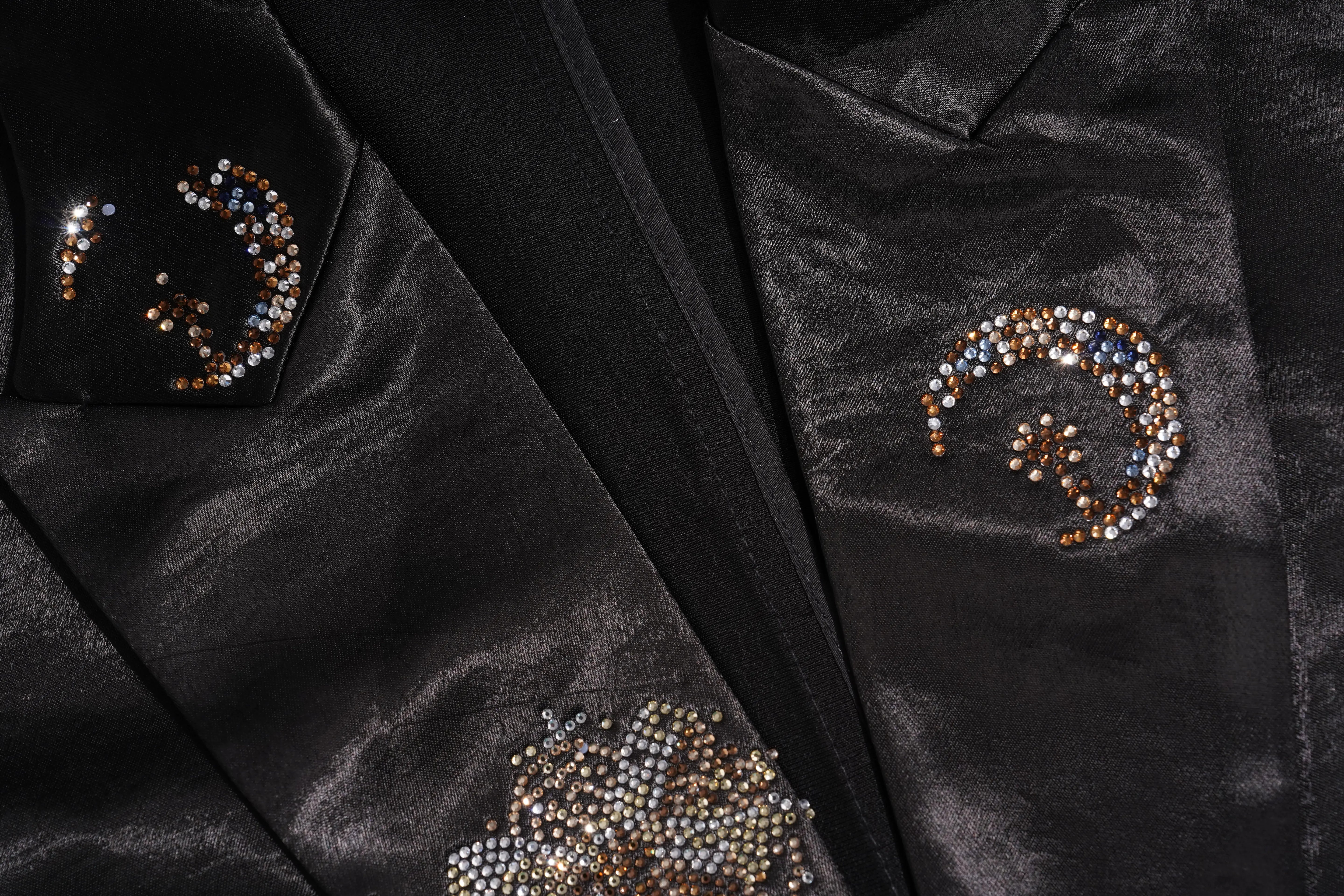 Close-up of a black satin jacket with three spiral patterns of rhinestone embellishments on the lapels and chest. TCH Rhinestone Bow Satin Blazer