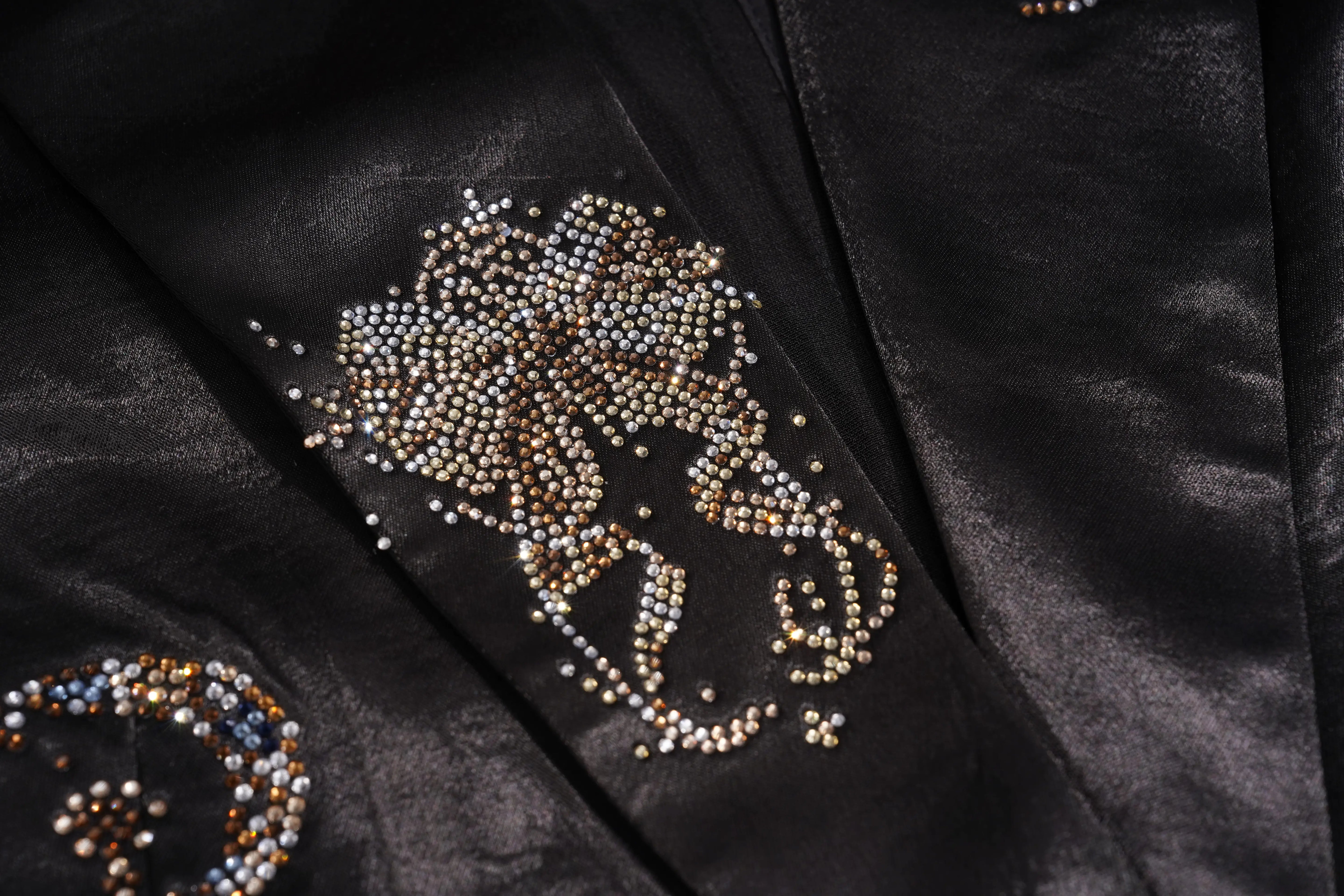 Close-up of a taupe-brown fabric embellished with dense floral patterns of small metallic rhinestones and sequins. TCH Rhinestone Bow Satin Blazer