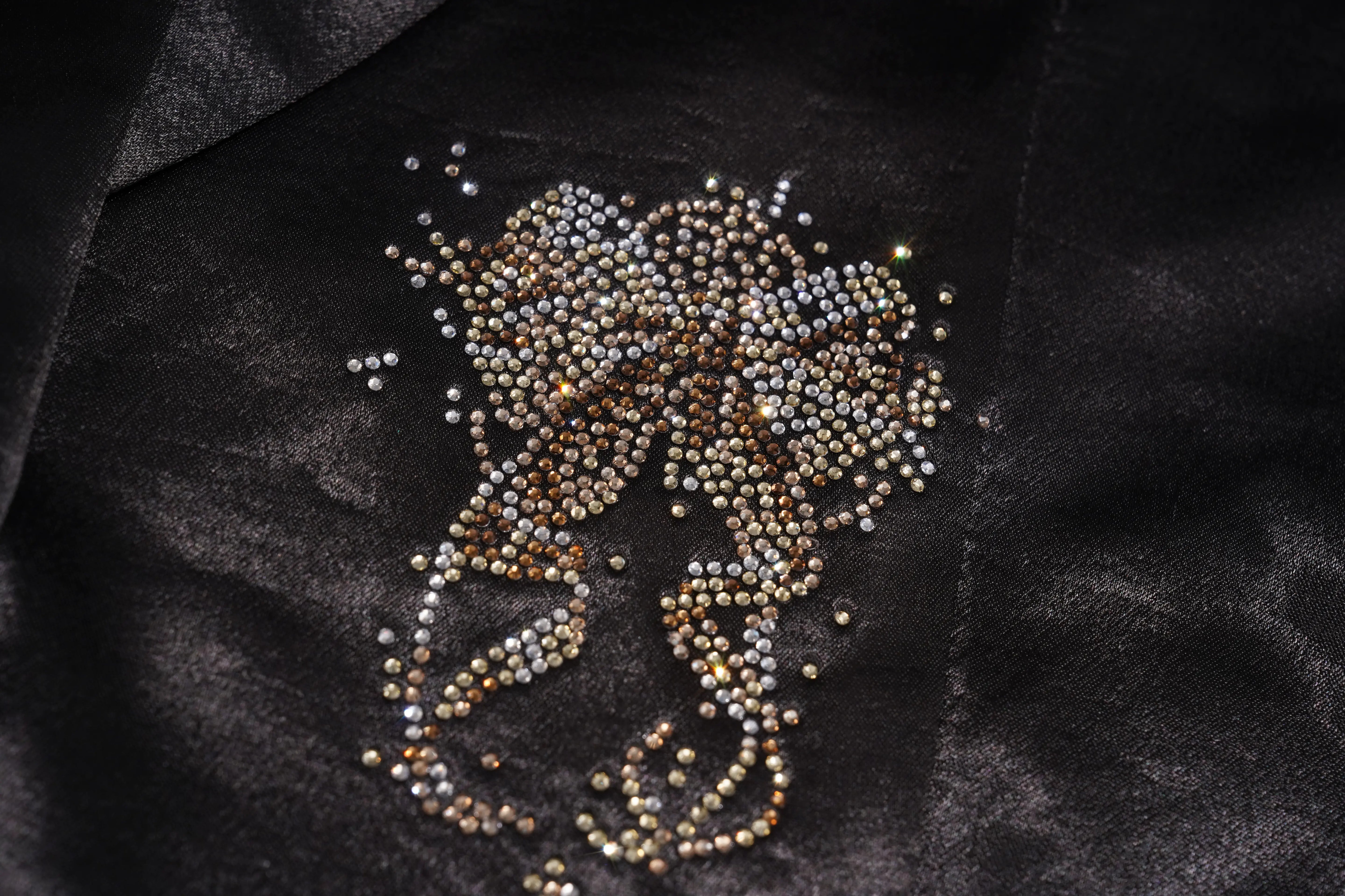 A close-up of a black fabric garment featuring an intricate, hand-embroidered or applique design of small metallic beads in silver, gold, and bronze tones. TCH Rhinestone Bow Satin Blazer