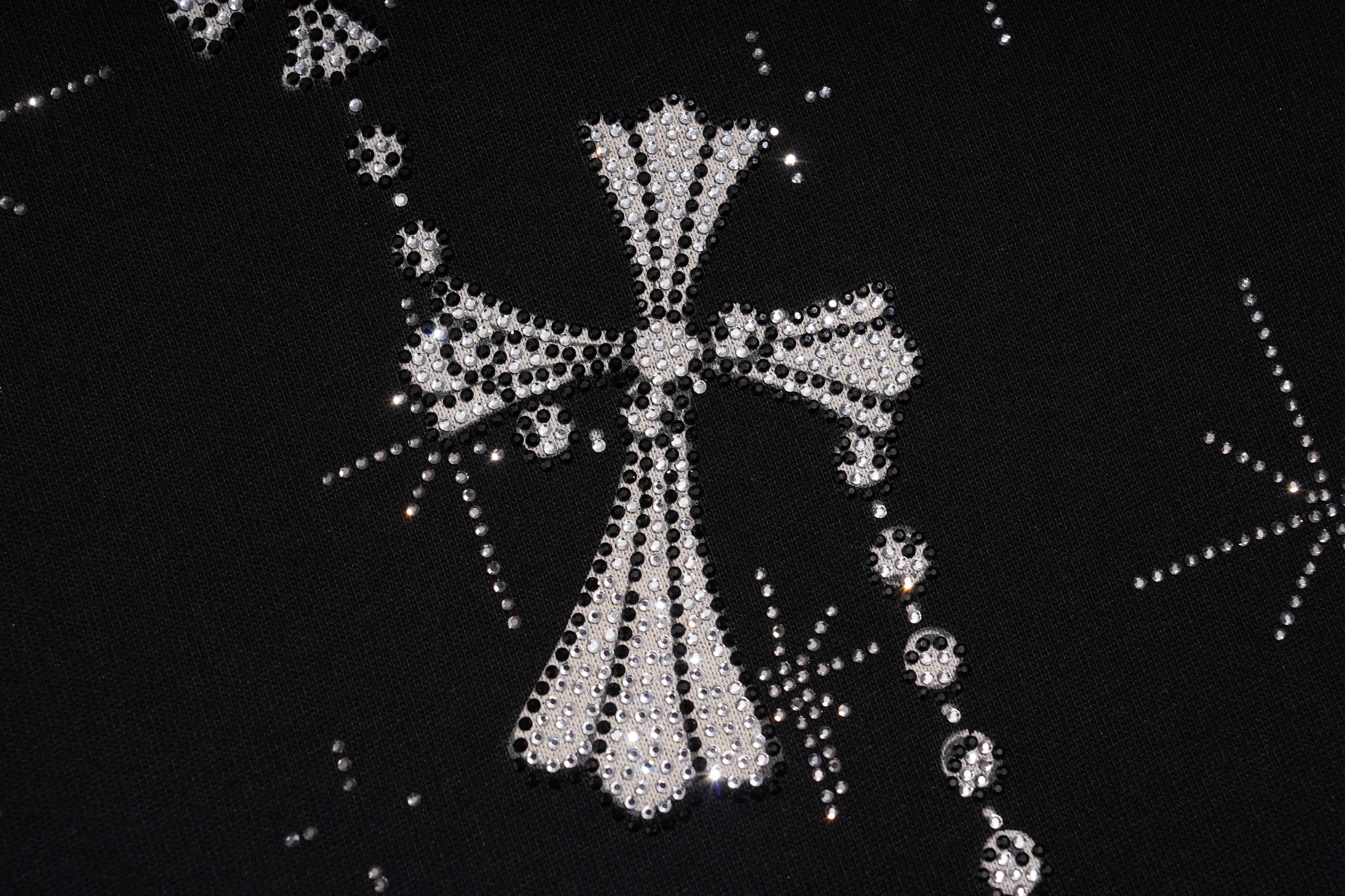 A close-up of a black garment or fabric decorated with a large silver rhinestone cross and smaller matching starburst and circular embellishments. TCH Rhinestone Bow Star Pattern Black T-Shirt