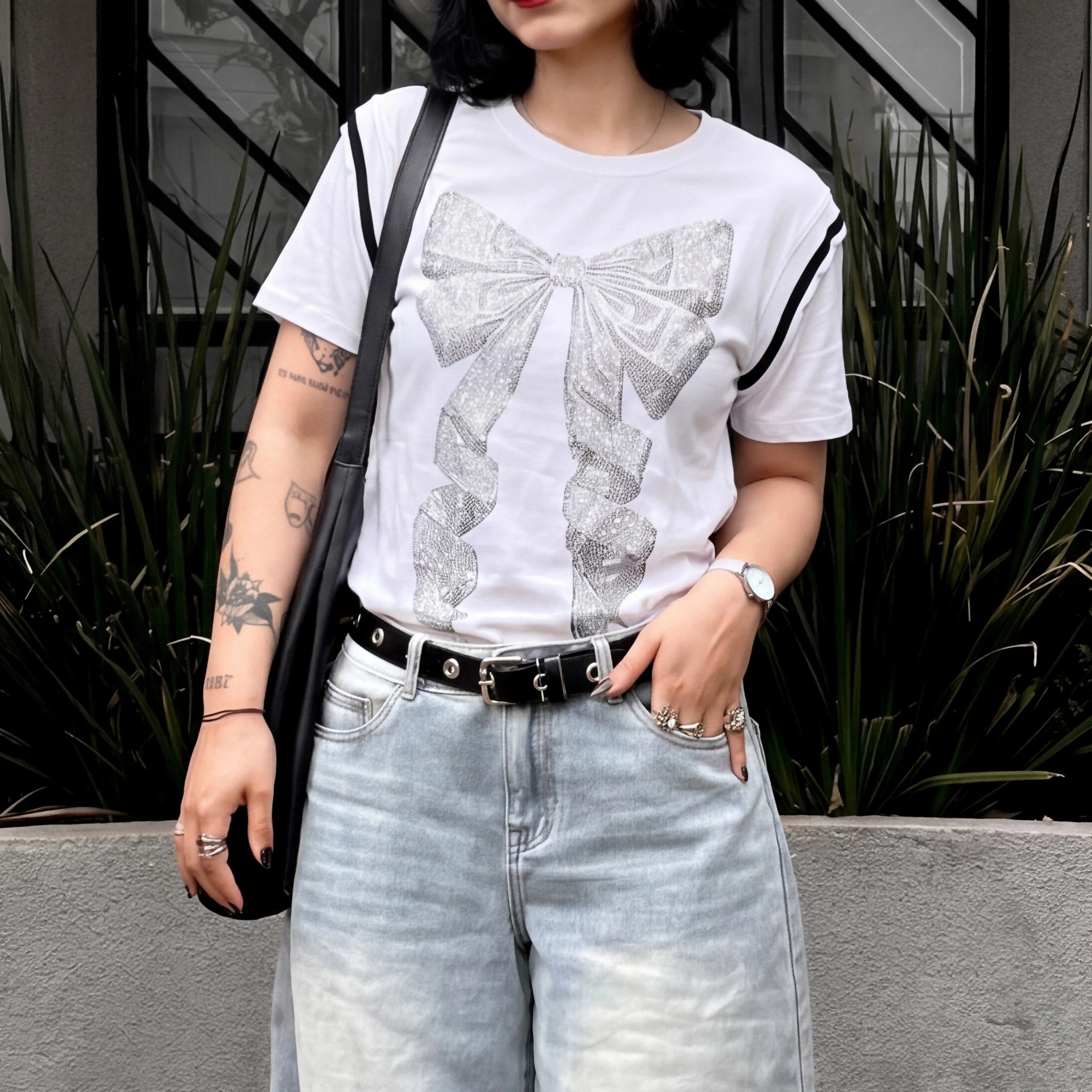 Person wearing a white t-shirt with a bow design and light blue jeans, standing outdoors. TCH Rhinestone Bow White T-Shirt