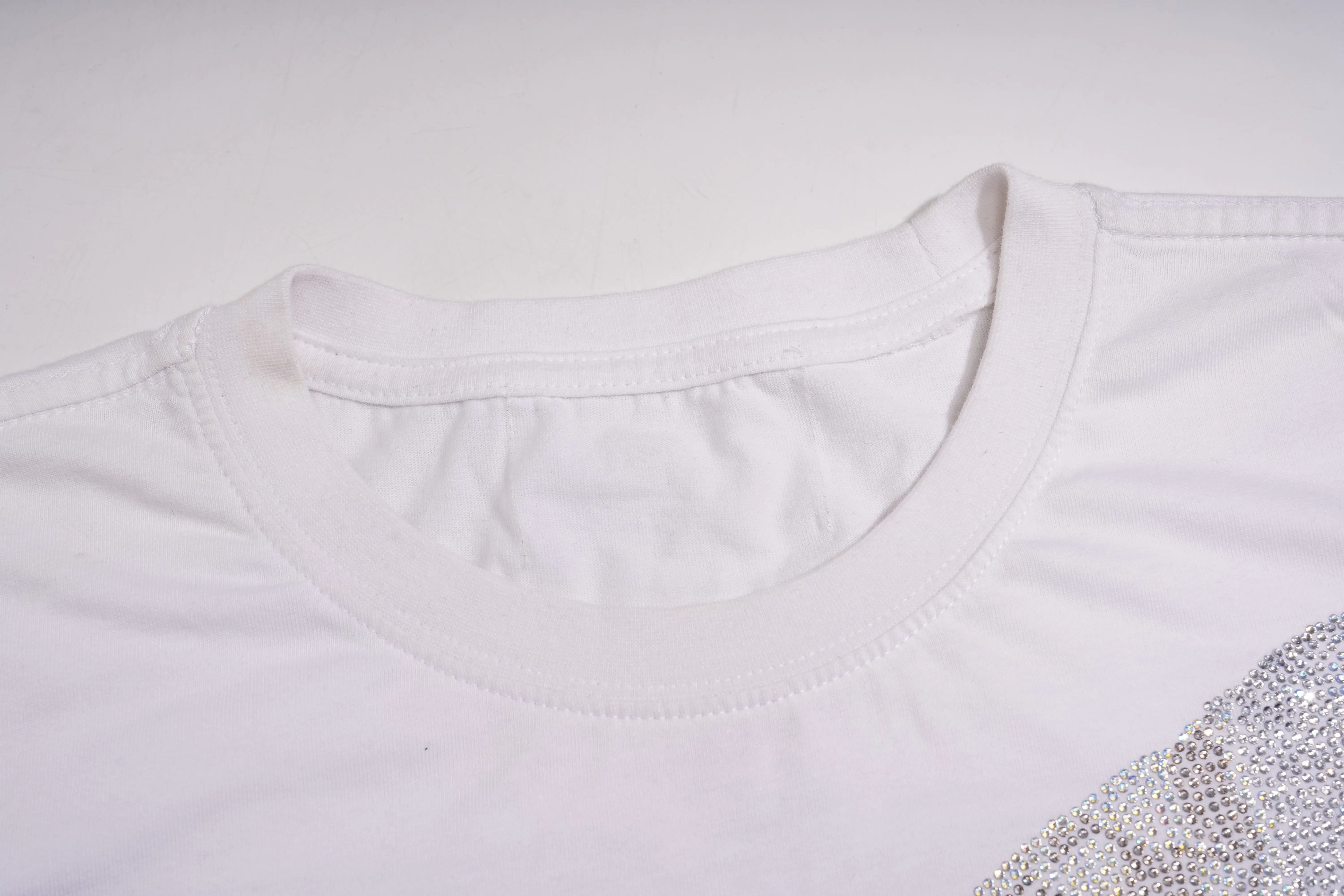 Close-up of a white garment with a decorative pattern on a light gray background, TCH Rhinestone Bow White T-Shirt