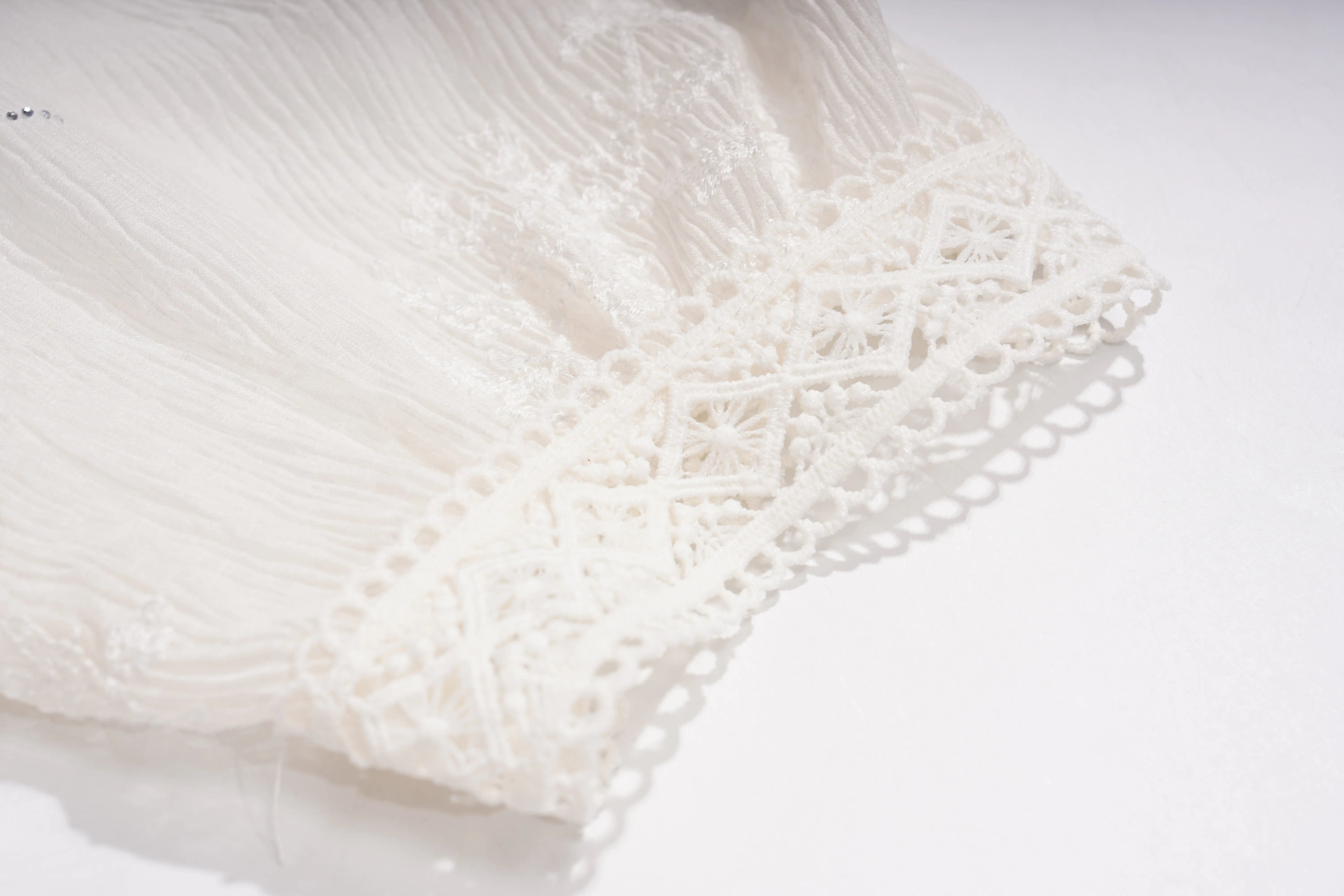 Close-up of a white lace and embroidered fabric detail, showing delicate crochet patterns and scalloped edges on a white background. TCH Rhinestone Butterfly Bow Lace Blouse