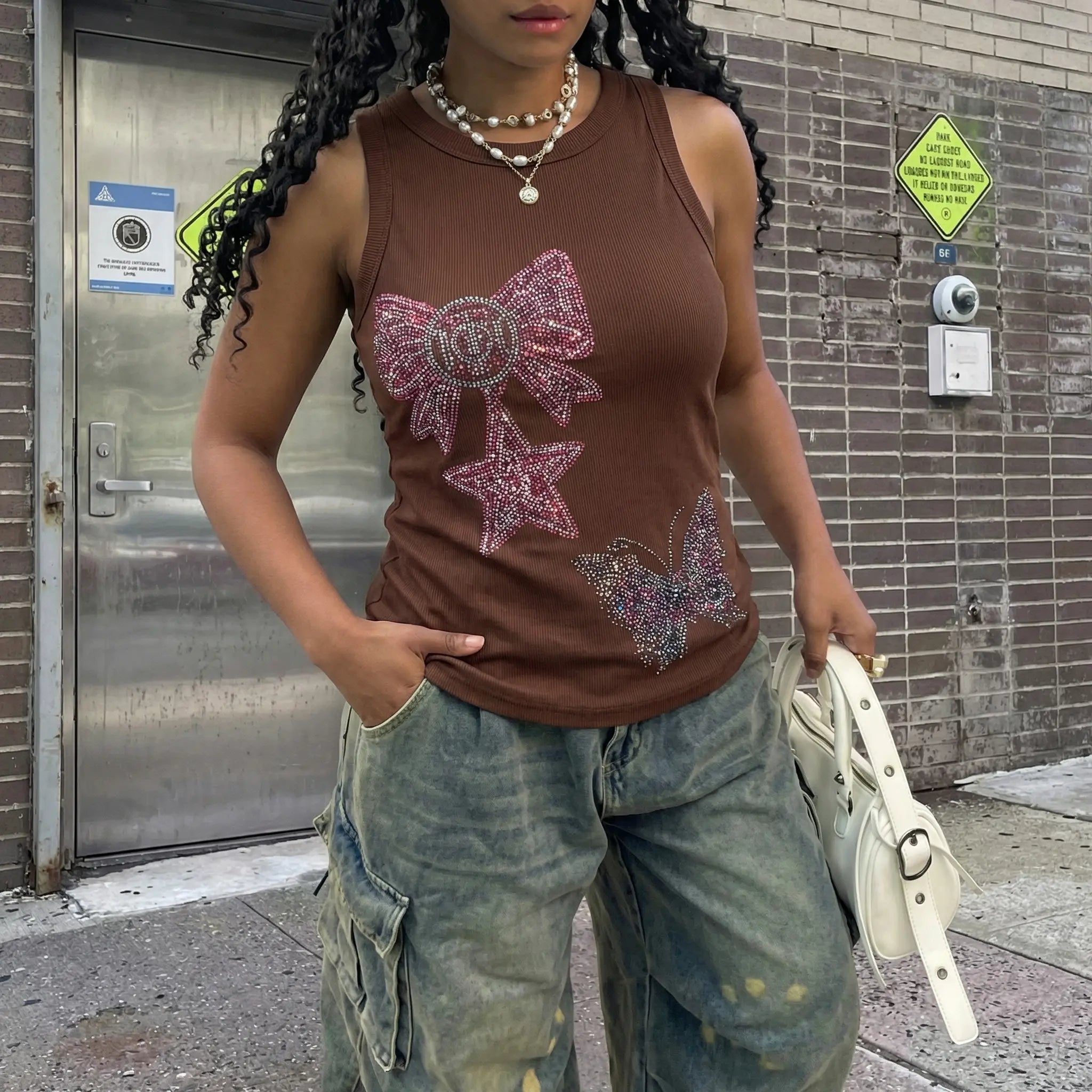Person wearing a brown tank top with pink butterfly designs in an urban setting. TCH Rhinestone Butterfly Bow Tank Top