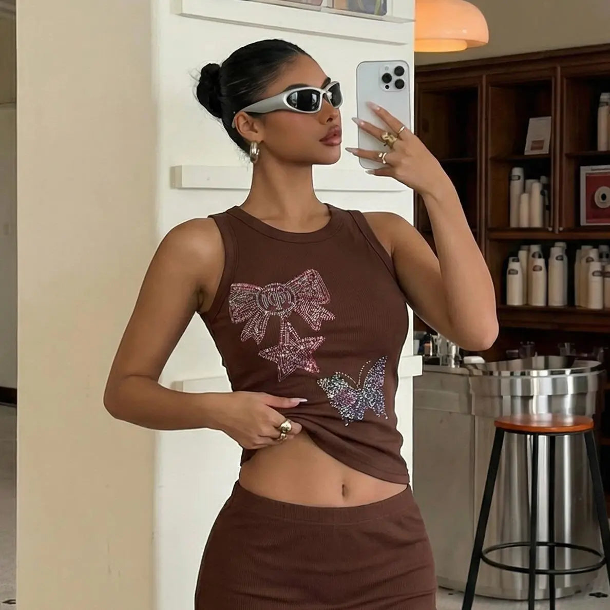 Woman taking a mirror selfie wearing a brown tank top with decorative bows and a skirt in a kitchen. TCH Rhinestone Butterfly Bow Tank Top
