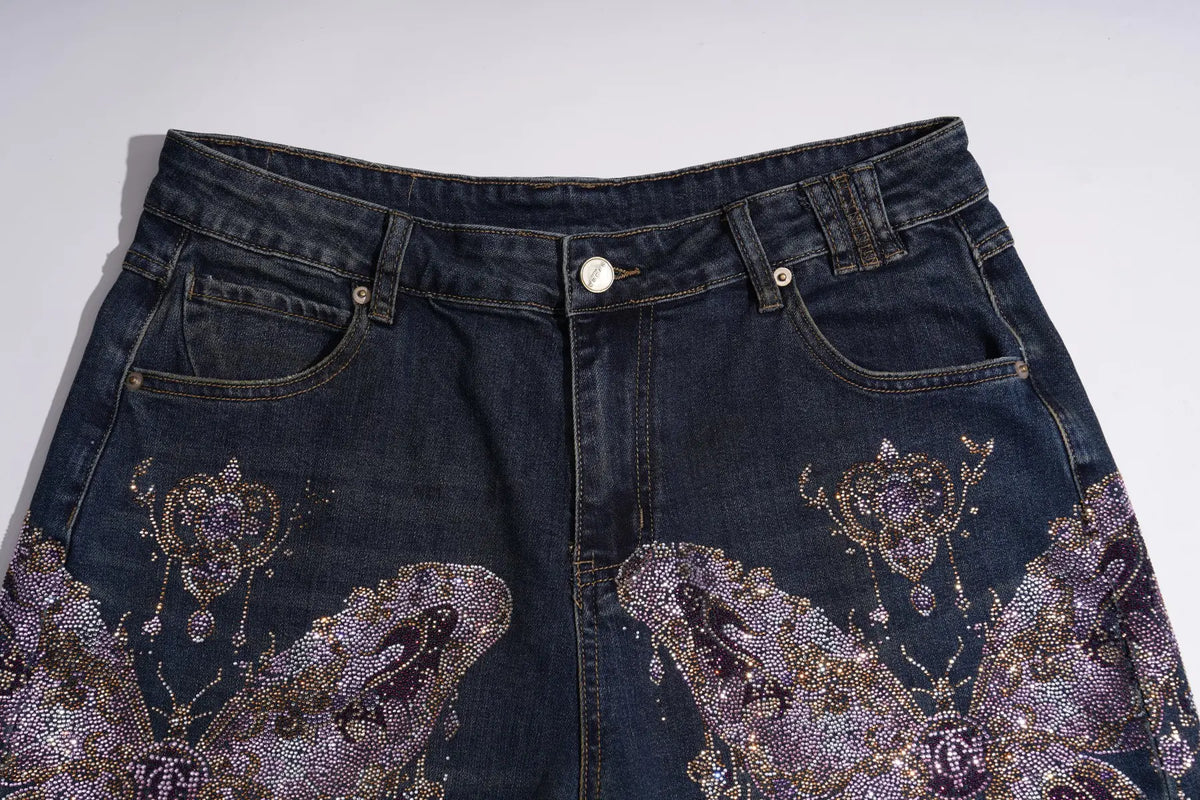 Dark blue denim jeans featuring intricate purple and gold butterfly embellishments on the front pockets and thighs, shown against a plain light gray background. TCH Rhinestone Butterfly Charm Wide-Leg Denim Jeans