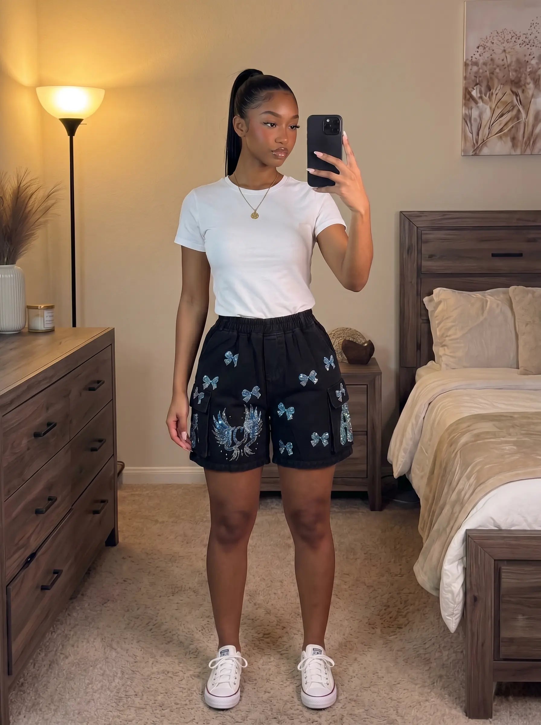 A woman takes a mirror selfie in a bedroom, wearing a white short-sleeve t-shirt, black shorts with blue and white butterfly prints, and white sneakers. TCH Rhinestone Butterfly & Dragon Graphic Black Cargo Shorts