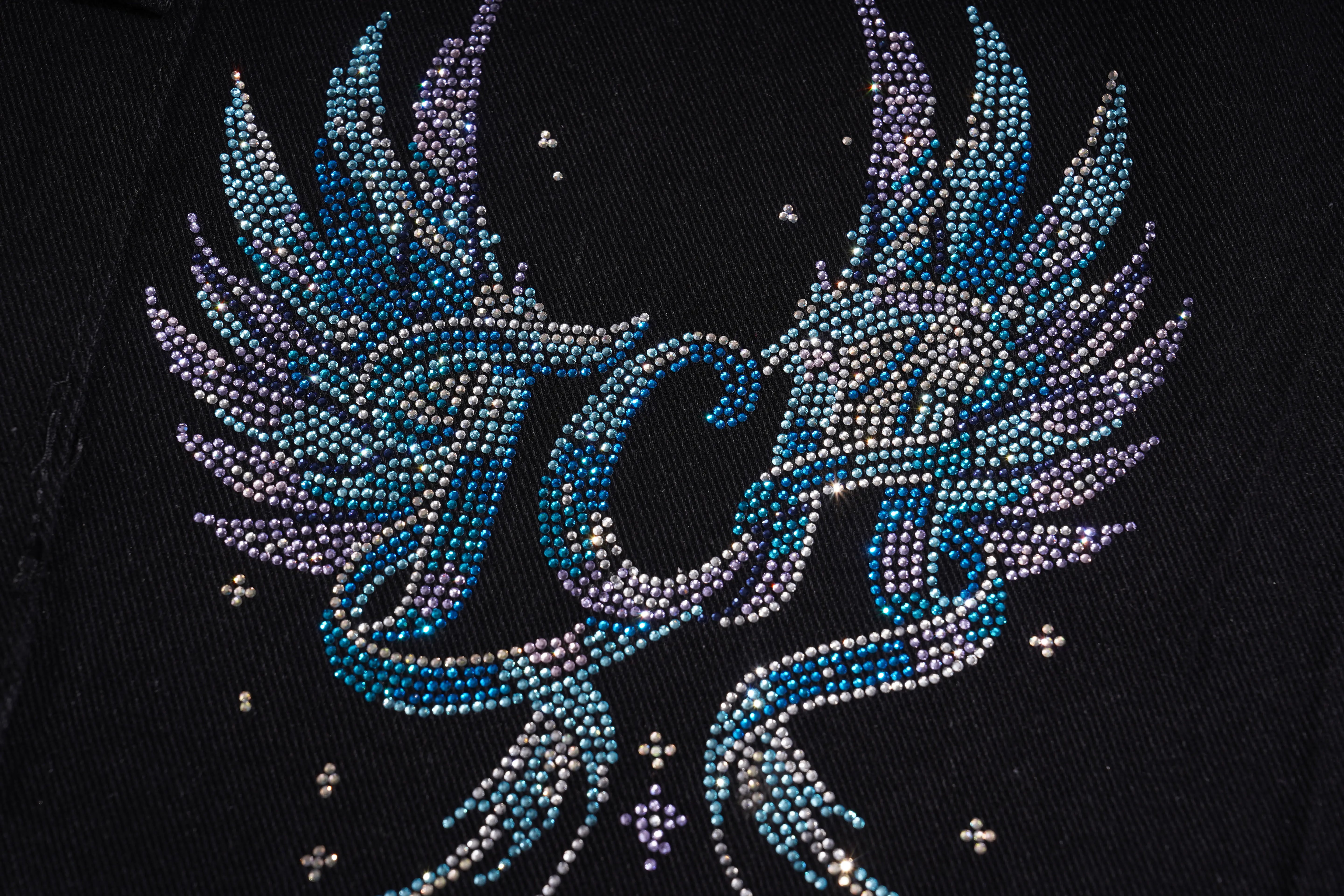 A close-up of a black fabric item featuring a large, detailed rhinestone winged monogram design in shades of blue, purple, and silver. TCH Rhinestone Butterfly & Dragon Graphic Black Cargo Shorts
