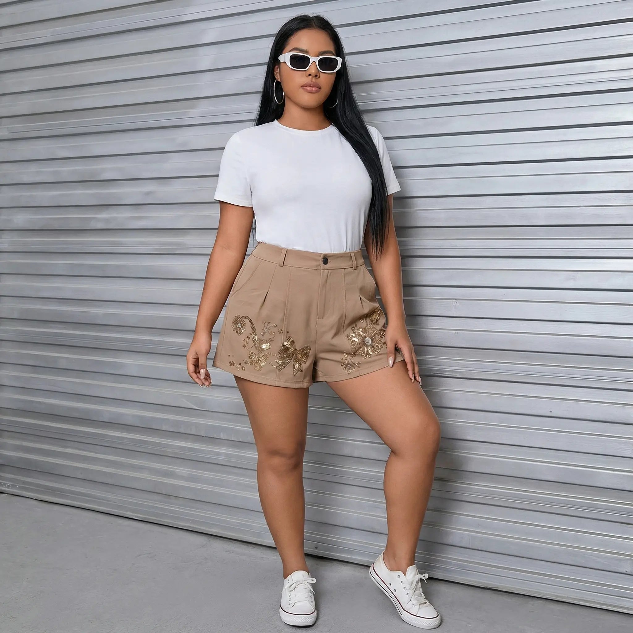 A woman stands in front of a gray metal roll-up door wearing a white short-sleeve crewneck top, beige shorts with gold sequin embroidery, and white sneakers. TCH Rhinestone Butterfly Floral Embellished Tailored Shorts