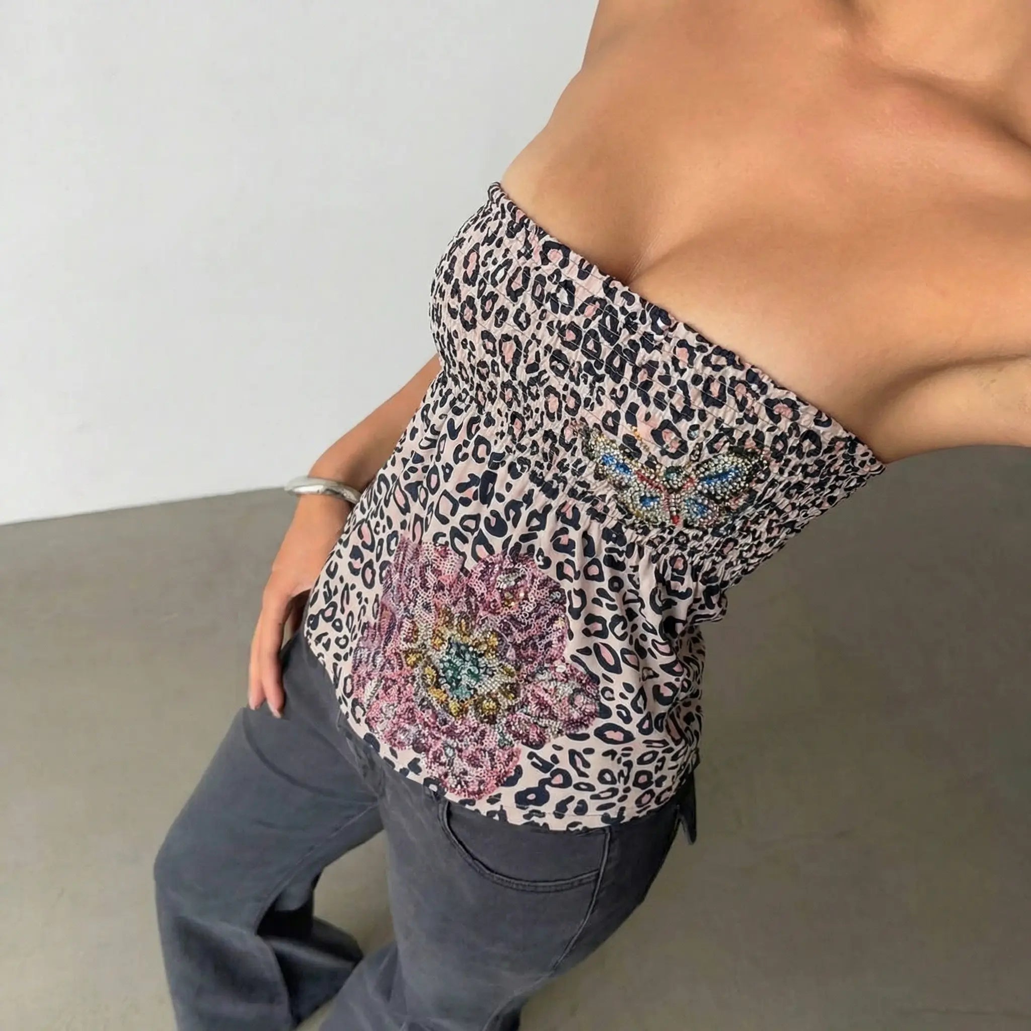 Person wearing a leopard print top with floral embellishments and gray pants. TCH Rhinestone Butterfly & Floral Leopard Tube Top