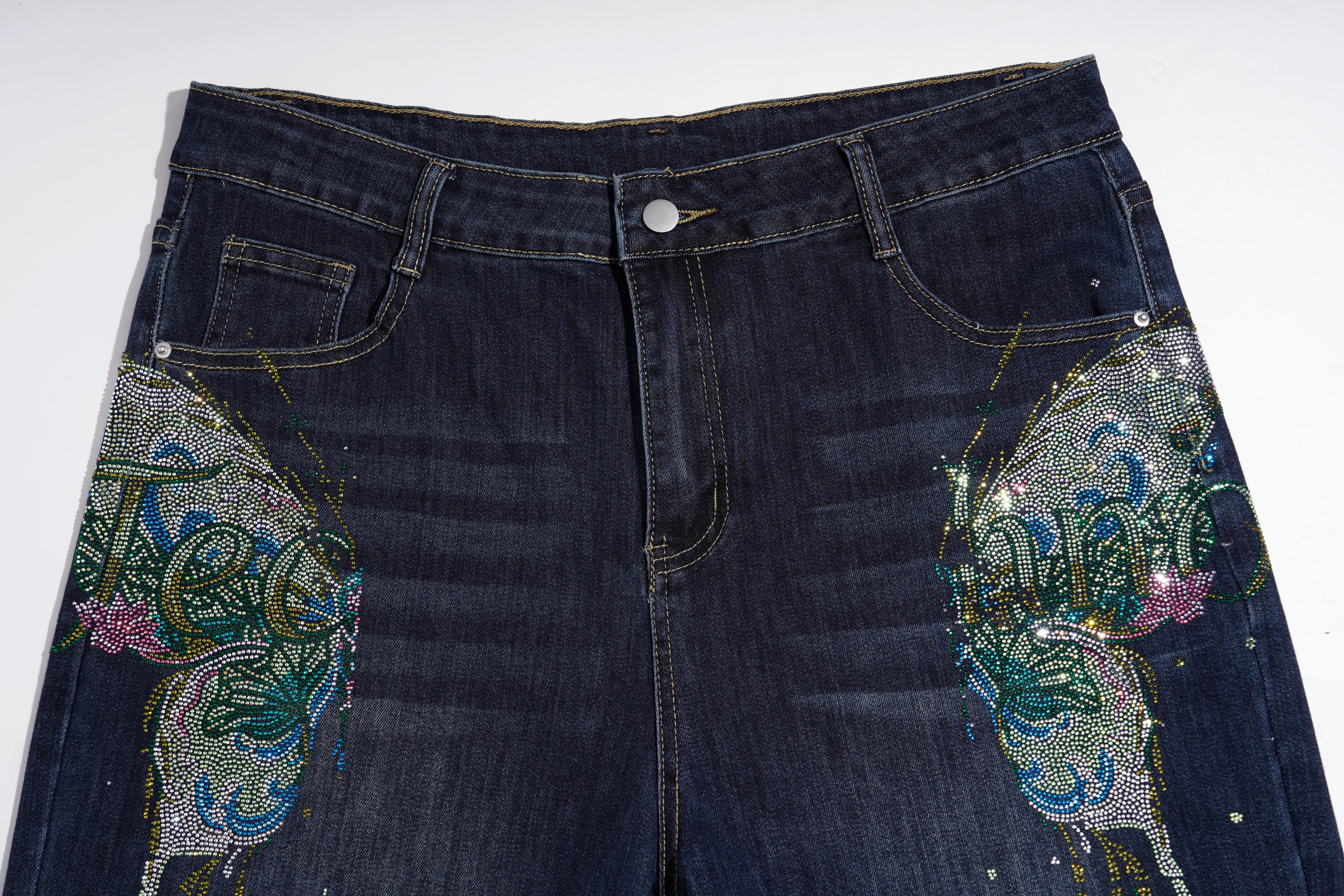 Dark blue denim jeans featuring large, intricate butterfly embellishments on both sides, decorated with sequins, rhinestones, and beads in green, blue, pink, and gold. TCH Rhinestone Butterfly Graphic Wide-Leg Jeans