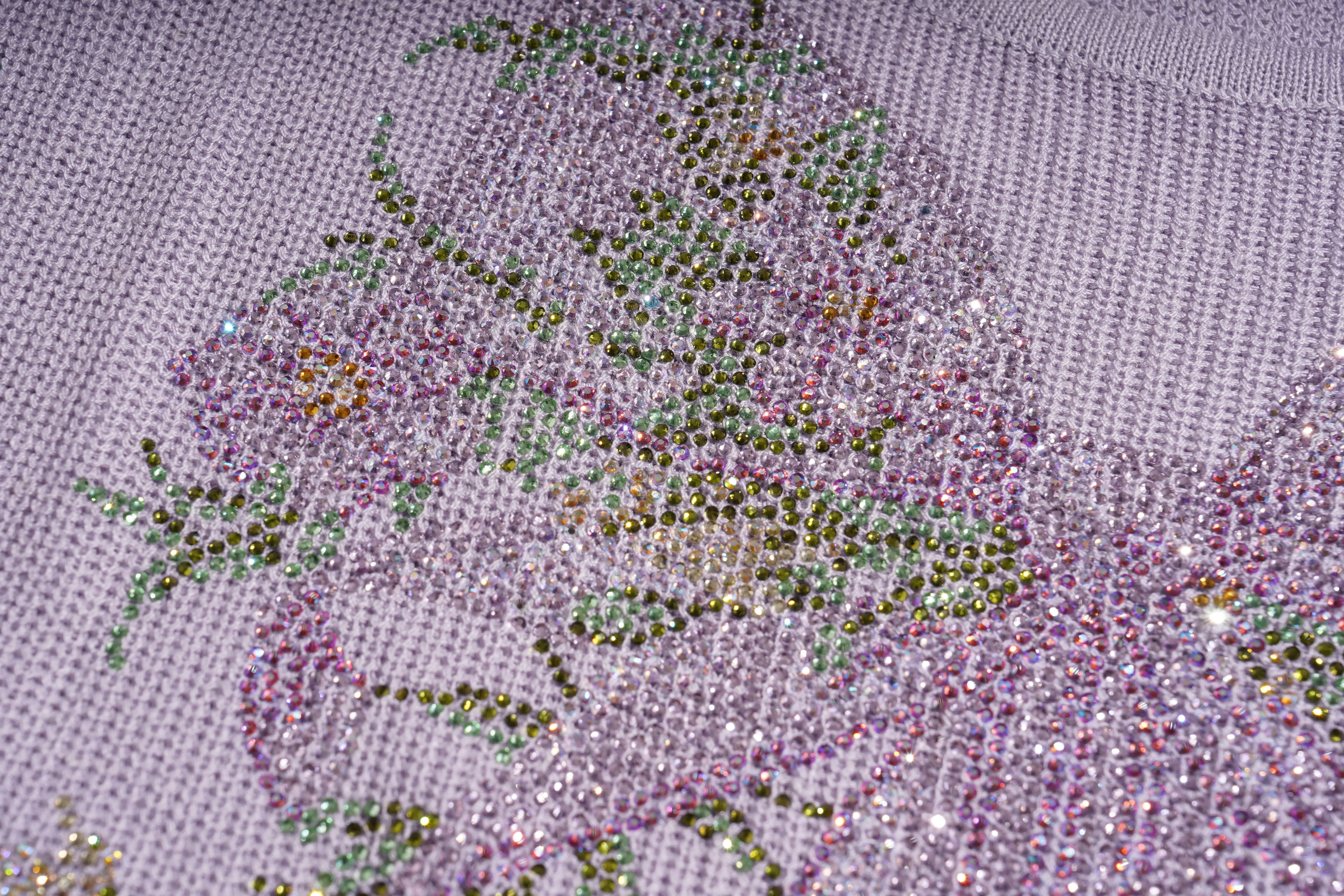 Close-up of a lavender knit fabric embellished with iridescent rhinestones forming a floral pattern. TCH Rhinestone Butterfly Knit Twist Top