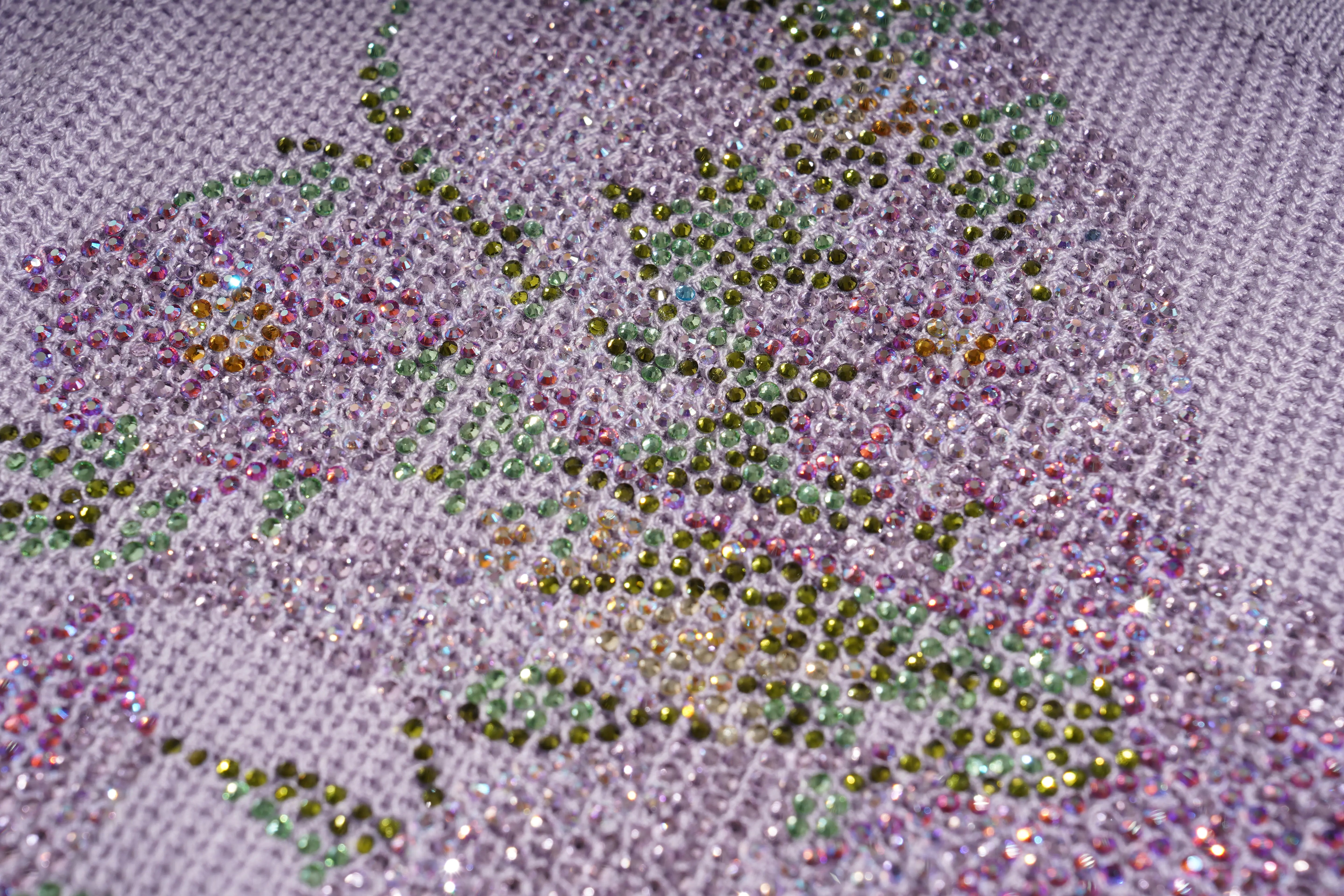 Close-up of a floral needlepoint canvas with beads and rhinestones applied to a light lavender mesh, featuring pink, green, and iridescent accents. TCH Rhinestone Butterfly Knit Twist Top