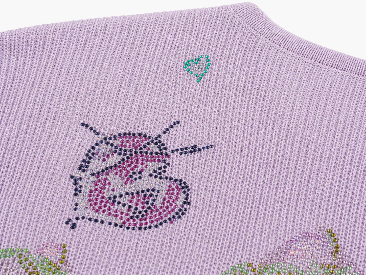 Close-up of a light lavender knit sweater featuring a decorative insect motif made of pink, purple, and dark gray rhinestones, with a small teal heart detail near the neckline. TCH Rhinestone Butterfly Knit Twist Top
