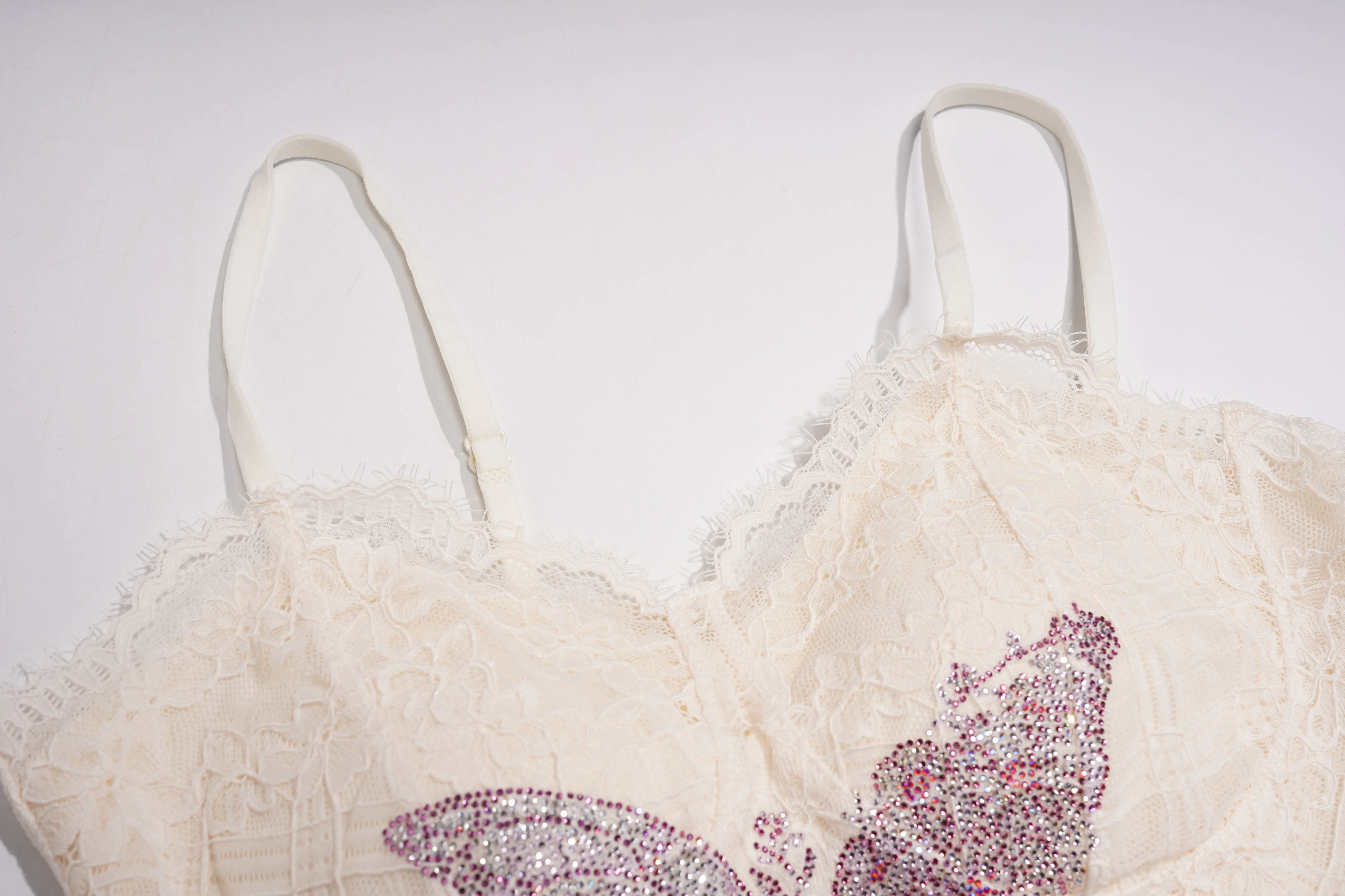 An off-white lace bra with thin straps and a large pink and silver rhinestone butterfly applique on the front, shown against a plain light background. TCH Rhinestone Butterfly Lace Cami Top