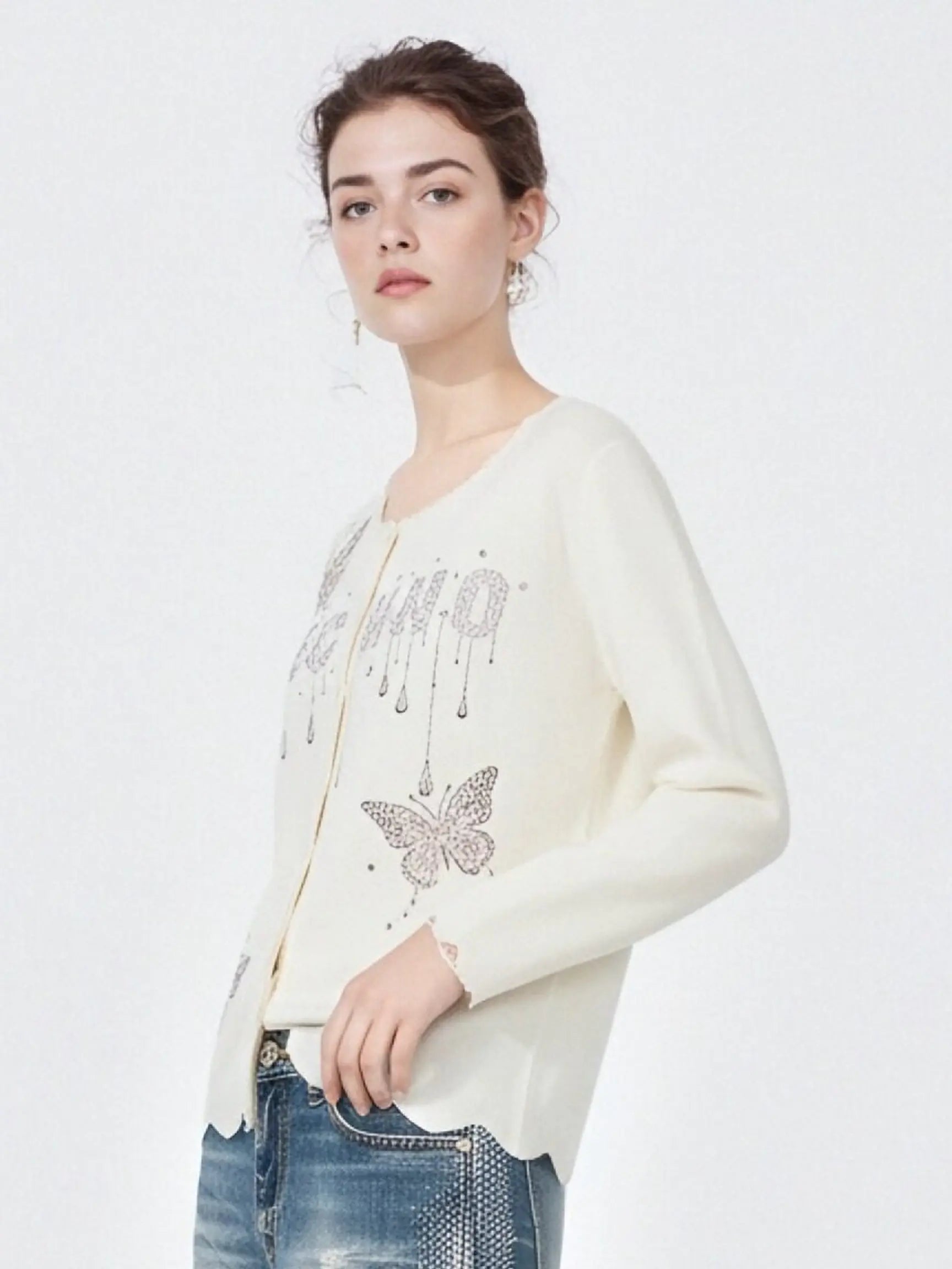 Woman wearing a cream cardigan with butterfly design on a white background, TCH Rhinestone Butterfly Logo Knit Cardigan