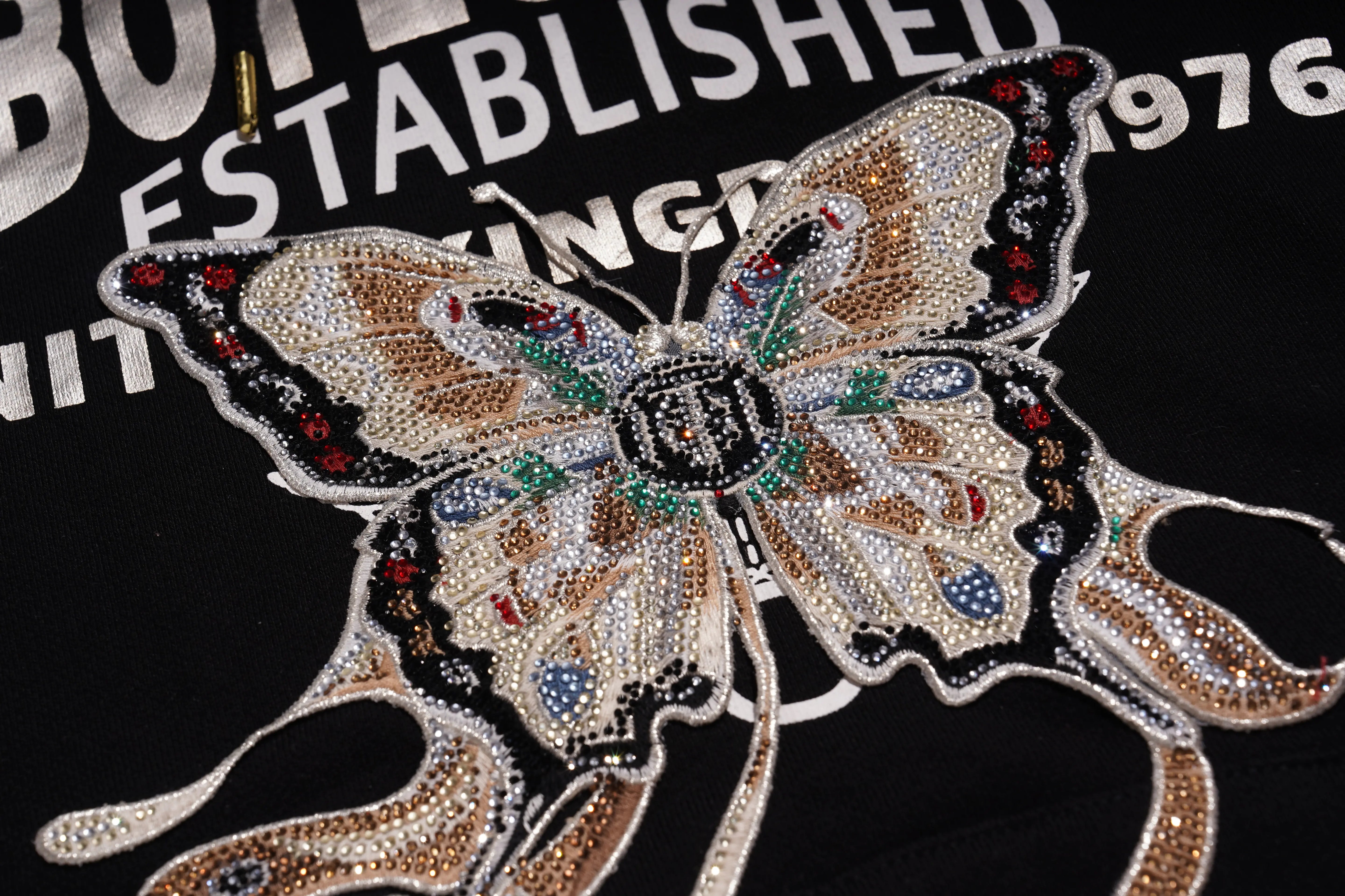 Butterfly-shaped decorative patch with rhinestones on a black background with text. TCH Rhinestone Butterfly & Peony Embroidered Hoodie