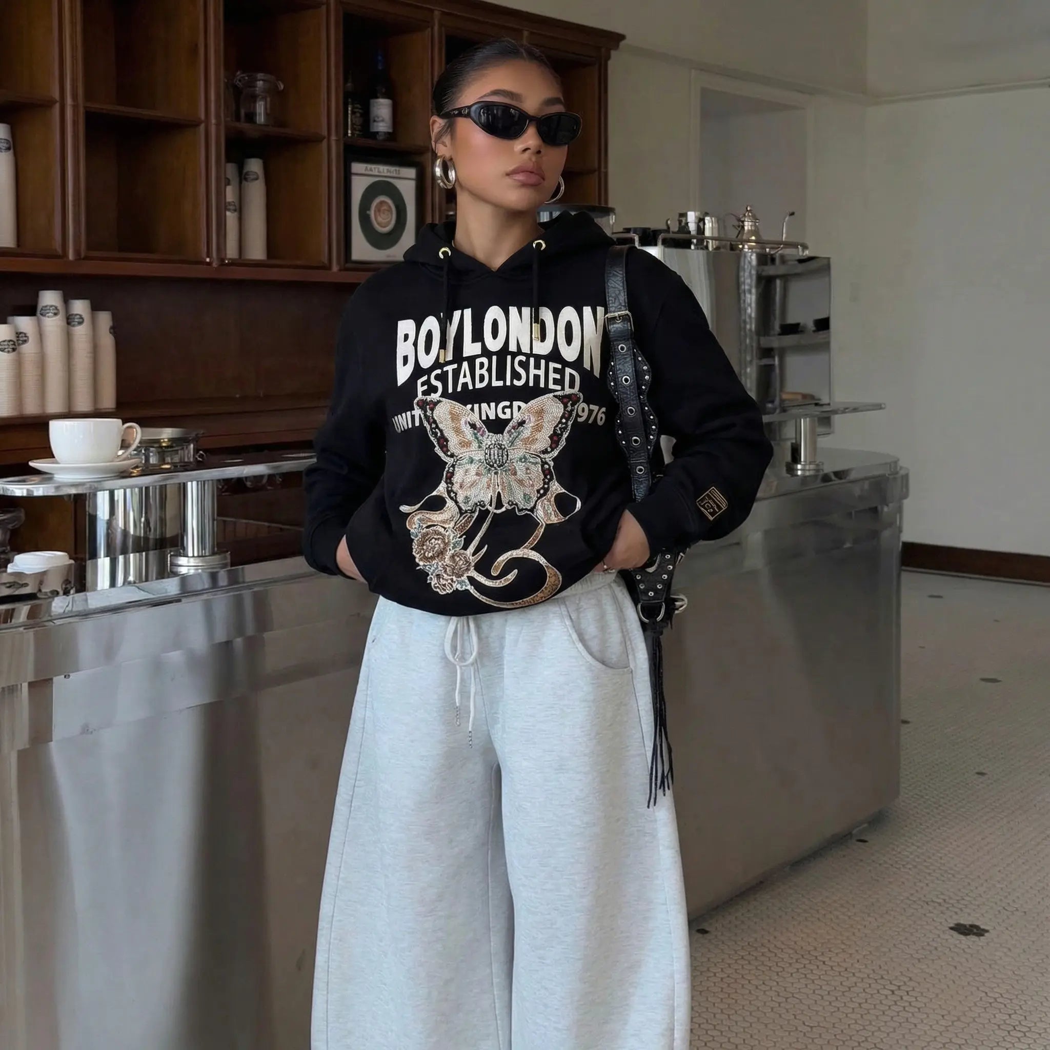 Person wearing a black hoodie with 'BOYLONDON' branding in a kitchen setting， TCH Rhinestone Butterfly & Peony Embroidered Hoodie