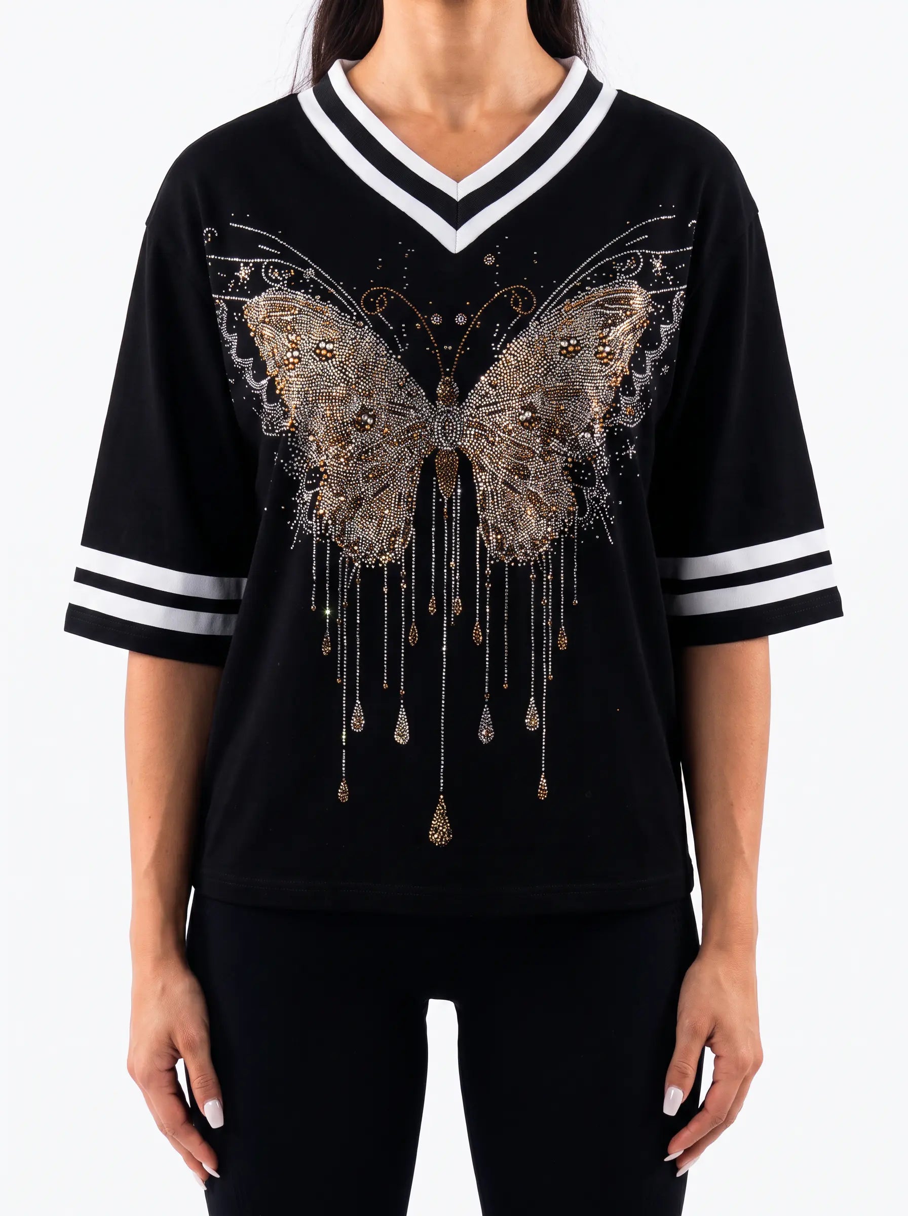 A woman wearing a black V-neck short-sleeve top with white stripes on the collar and sleeves, featuring a large metallic gold butterfly graphic with dangling details on the front. TCH Rhinestone Butterfly V-Neck Oversized Baseball T-Shirt