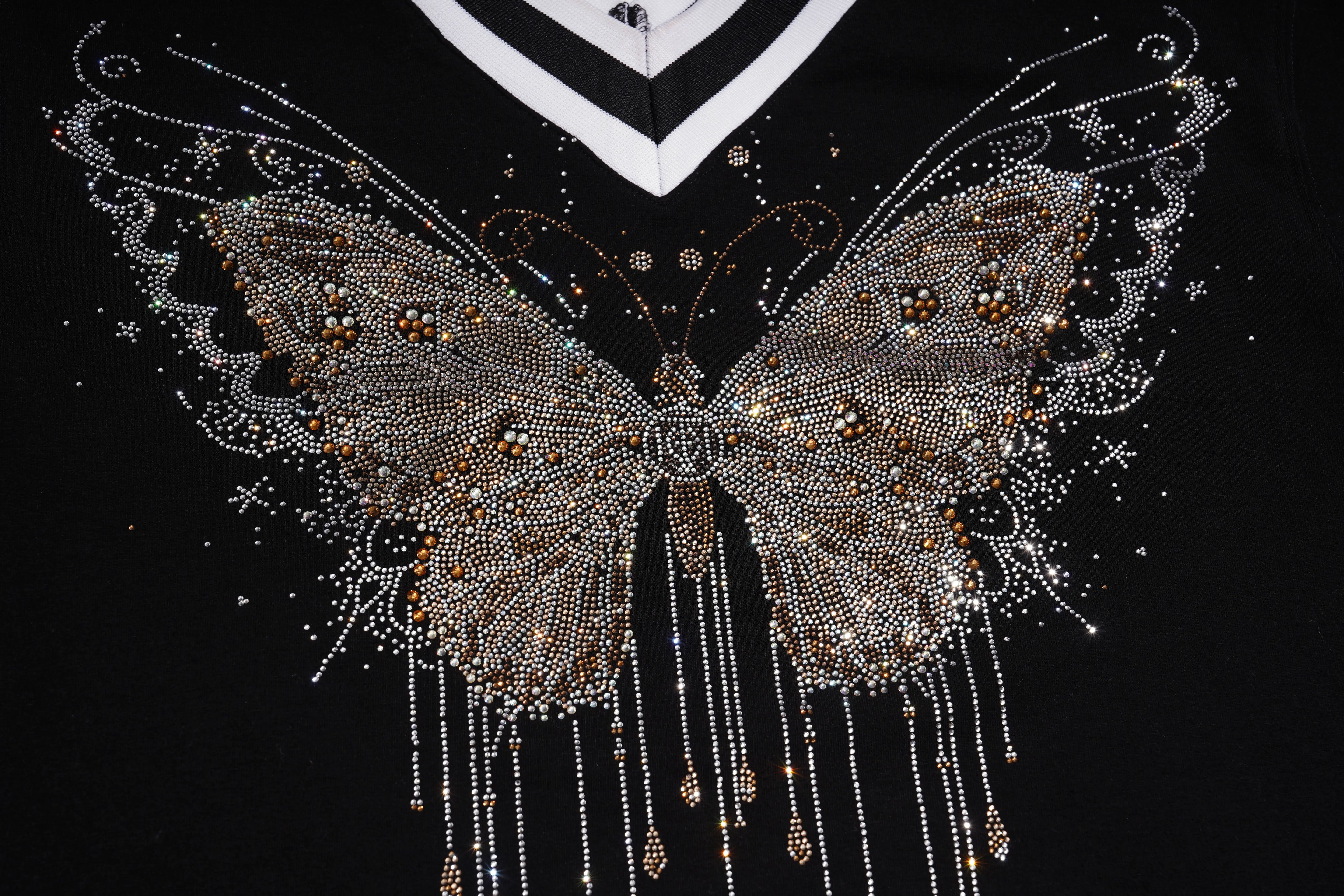 A close-up of a black V-neck top featuring an intricate rhinestone butterfly design on the chest, with dangling rhinestone chains and a white collar trim. TCH Rhinestone Butterfly V-Neck Oversized Baseball T-Shirt