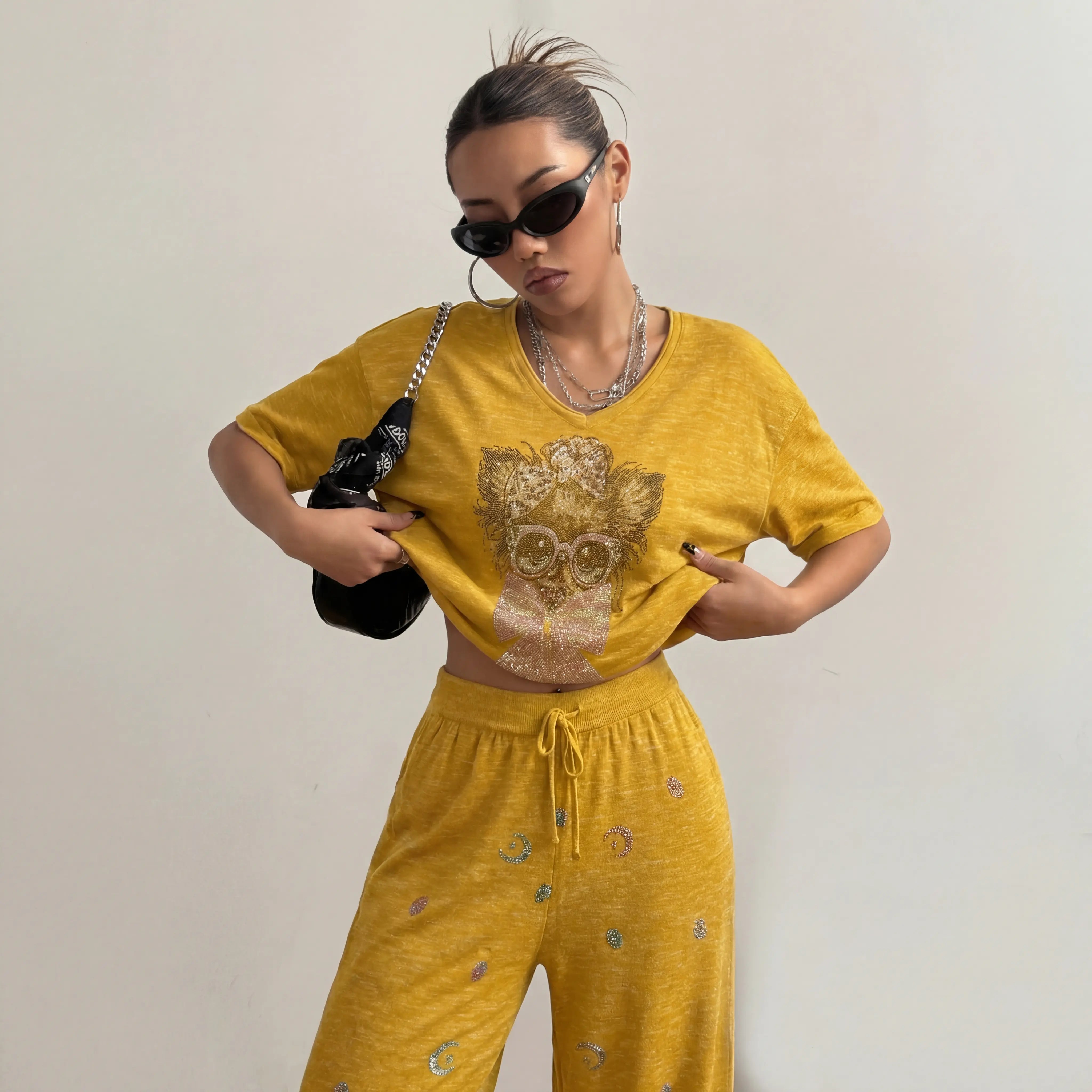 Woman wearing a yellow outfit with a decorative design, holding a black bag against a plain background. TCH Rhinestone Chihuahua Galaxy Set
