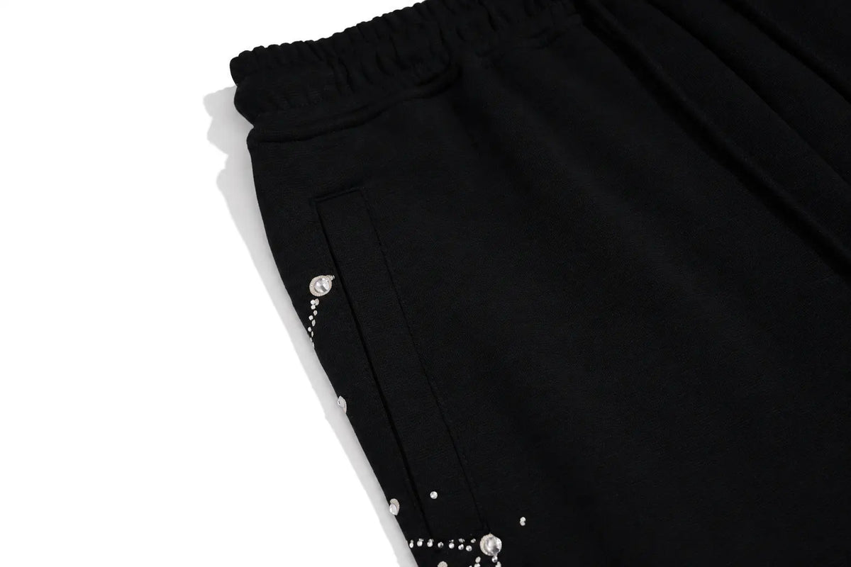 Close-up of black pleated fabric with a gathered elastic waistband and small silver rhinestone embellishments along the side, photographed on a white background. TCH Rhinestone Constellation Straight-Leg Sweatpants