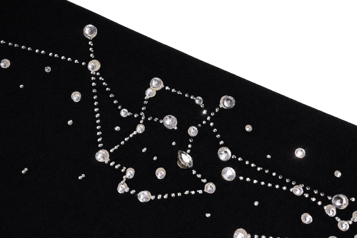 A close-up of a black fabric embellished with silver rhinestone bead lines and clear faceted crystals, set against a white background. TCH Rhinestone Constellation Straight-Leg Sweatpants