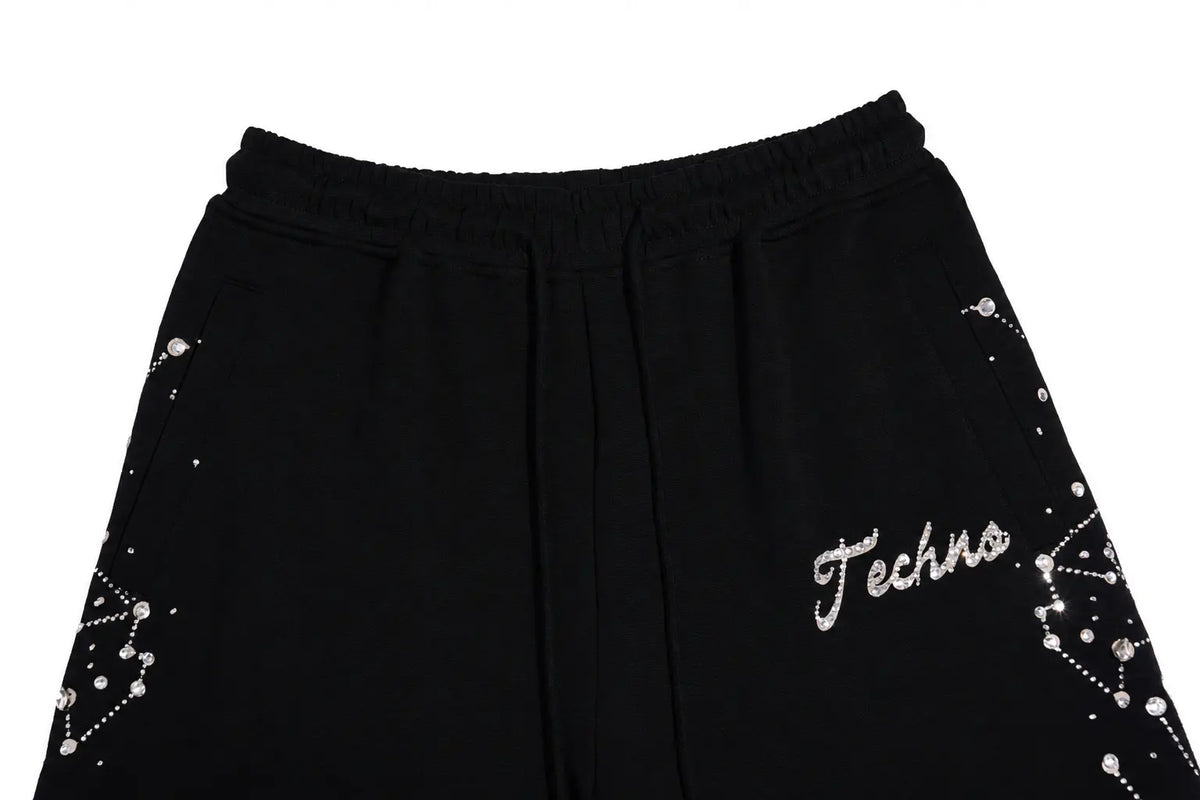 Black sweatpants featuring an elastic waistband, side pockets, and silver rhinestone embellishments on the sides, with 'Techno' embroidered in silver on the lower right leg. TCH Rhinestone Constellation Straight-Leg Sweatpants
