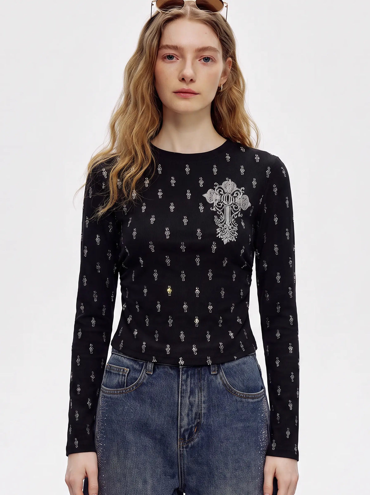 A model wearing a light blue denim jacket with various embroidered patches, including a teddy bear on the left chest and cherries on the sleeve, styled over a white t-shirt and dark pants. TCH Rhinestone Cross Graphic Fitted Long Sleeve Top