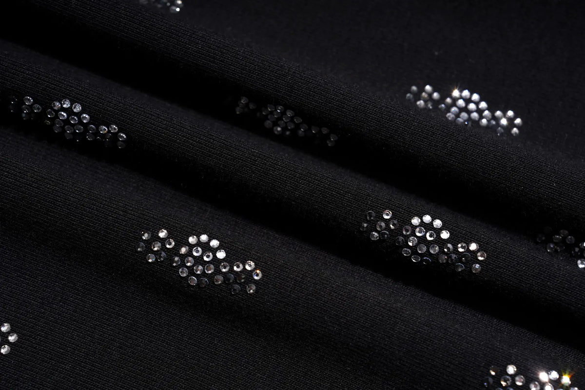 Close-up of a black knit fabric with repeating clusters of small silver rhinestones arranged in curved rows. TCH Rhinestone Cross Graphic Fitted Long Sleeve Top