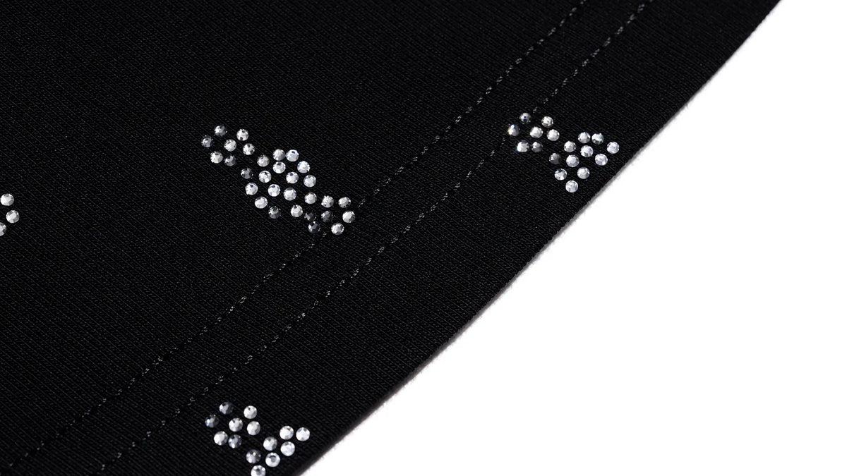 Close-up of a black fabric trim or ribbon with repeating silver rhinestone bow motifs along a diagonal seam on a white background. TCH Rhinestone Cross Graphic Fitted Long Sleeve Top
