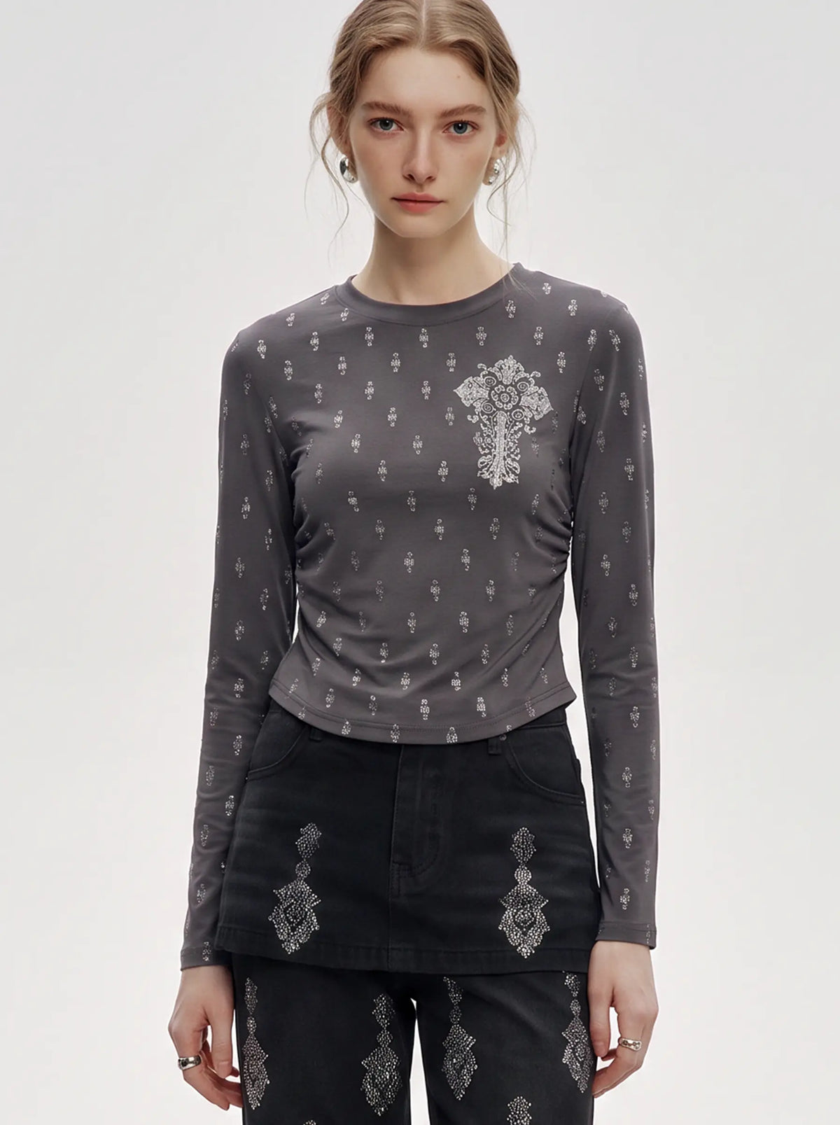 A model wearing a dark gray long-sleeve top with a white cross and small cross pattern, paired with black pants featuring white cross embroidery, against a light gray studio background. TCH Rhinestone Cross Graphic Fitted Long Sleeve Top