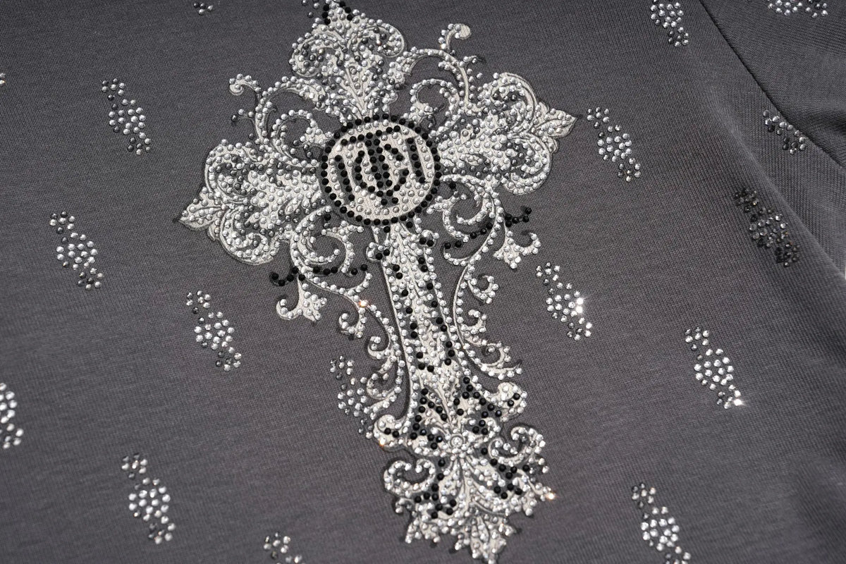 Close-up of a dark gray garment featuring an ornate silver and black beaded cross design with a circular monogram logo in the center. TCH Rhinestone Cross Graphic Fitted Long Sleeve Top