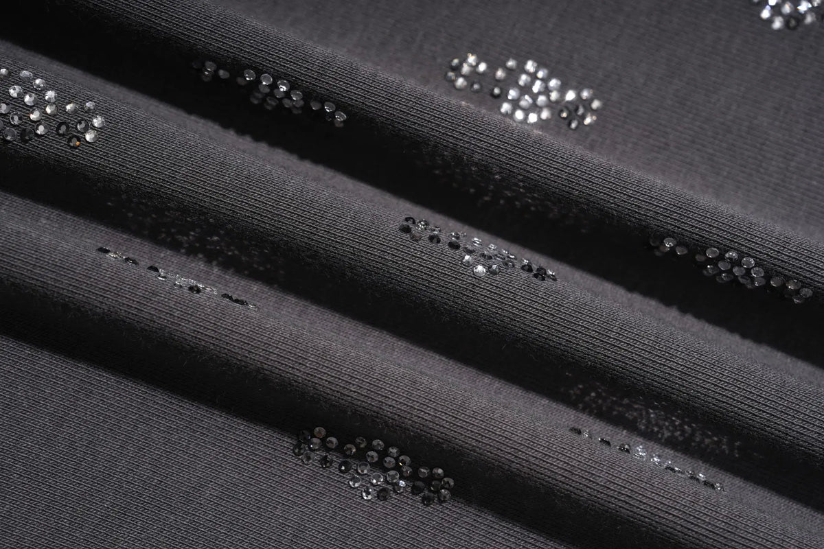 Close-up of a dark charcoal gray ribbed knit fabric with scattered small silver rhinestone embellishments. TCH Rhinestone Cross Graphic Fitted Long Sleeve Top