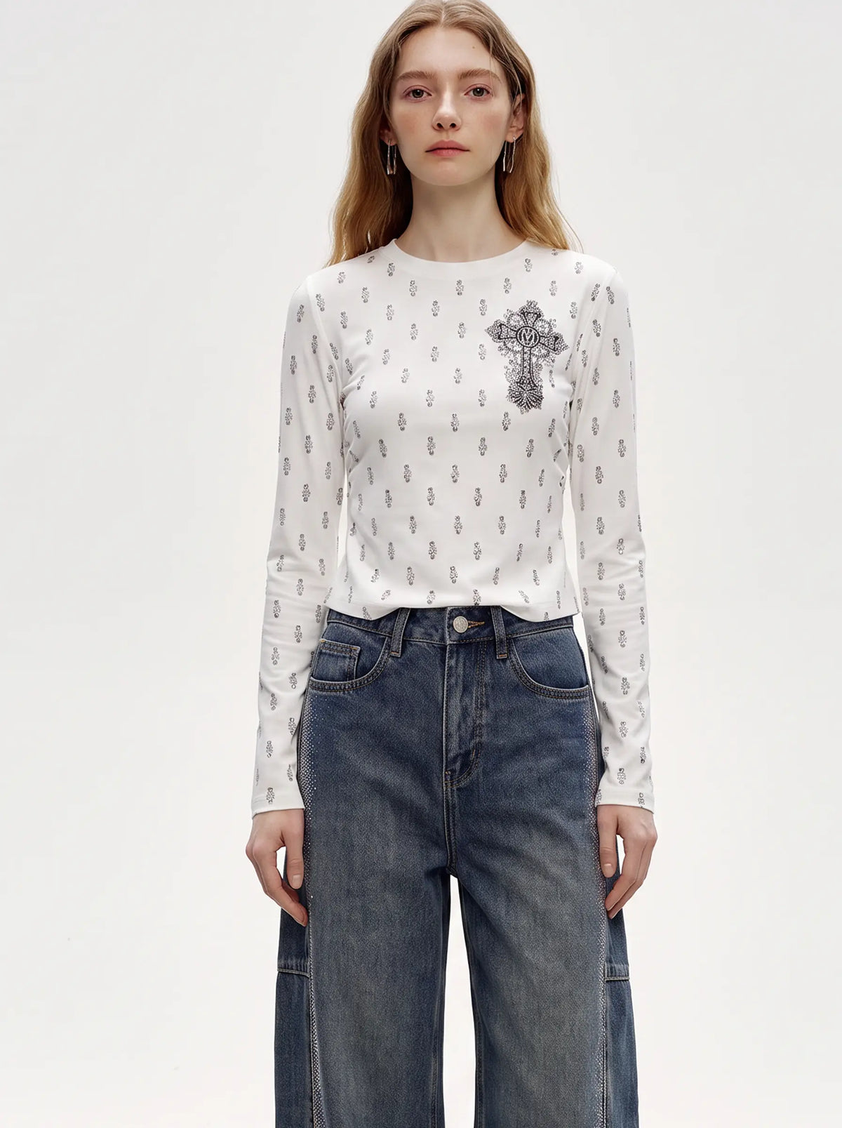 A woman modeling a white long-sleeve crewneck top with a small gray anchor pattern and a large gray anchor motif on the left chest, paired with high-waisted blue jeans against a light gray studio background. TCH Rhinestone Cross Graphic Fitted Long Sleeve Top