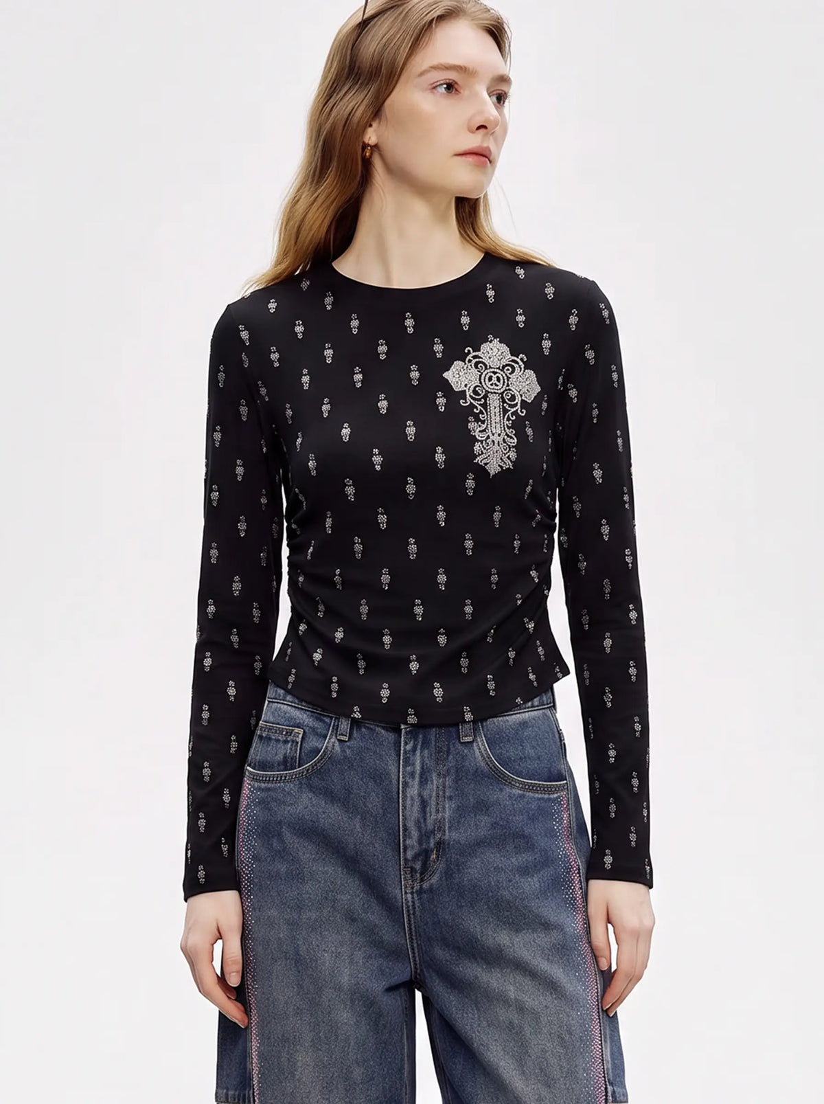 A woman modeling a black long-sleeve crewneck top with a small white gothic skull pattern and a large white ornate cross motif on the left chest, paired with blue jeans against a plain white studio background. TCH Rhinestone Cross Graphic Fitted Long Sleeve Top