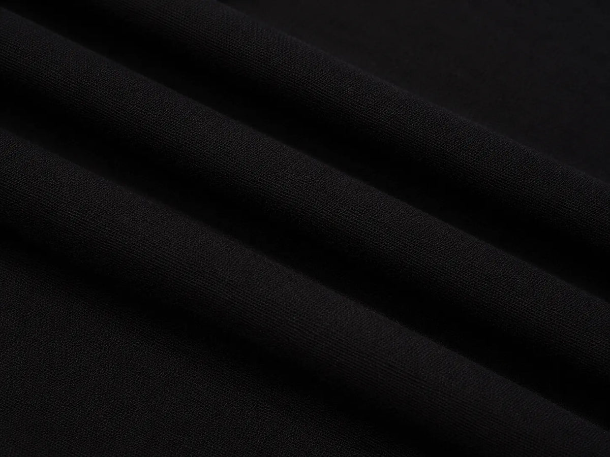 A close-up of draped black fabric with soft diagonal folds showing a fine woven texture. TCH Rhinestone Cross Pattern Black Long Sleeve T-Shirt