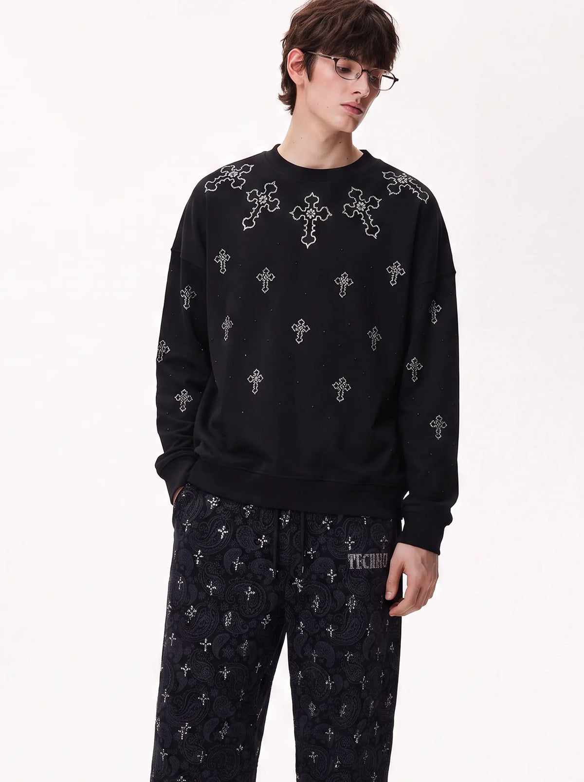 A model wearing a black crewneck sweatshirt and matching black pants with silver cross patterns, photographed against a plain white studio background. TCH Rhinestone Cross Pattern Black Long Sleeve T-Shirt