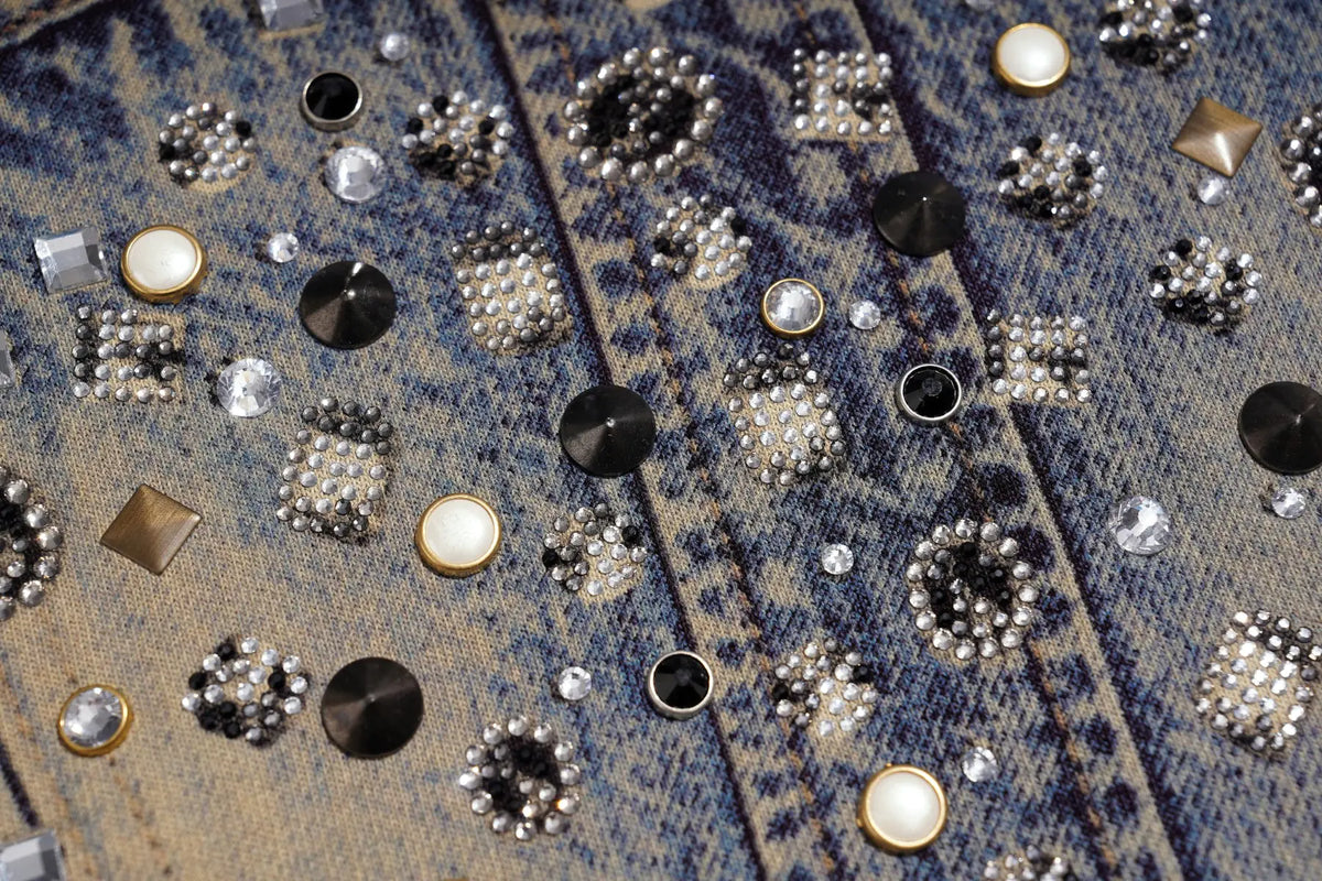 Close-up of a blue denim jacket covered with an intricate array of rhinestone and metallic stud embellishments. TCH Rhinestone Denim Corset Graphic Oversized T-Shirt